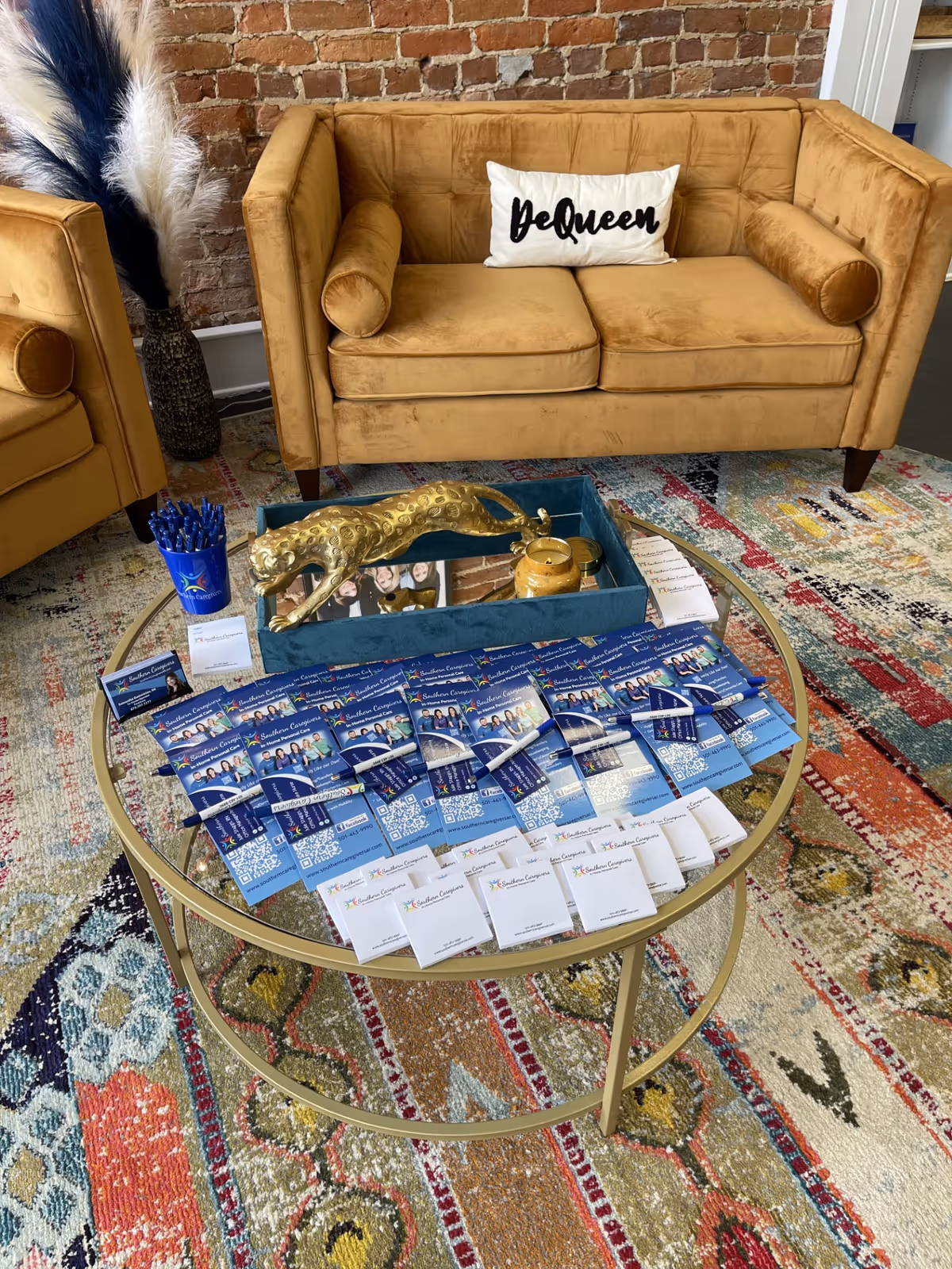Tan sofa with decorative pillow, glass coffee table laden with brochures in a colorful lounge.