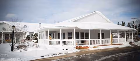 Snow blankets a white, single-story building with a wide wraparound porch.