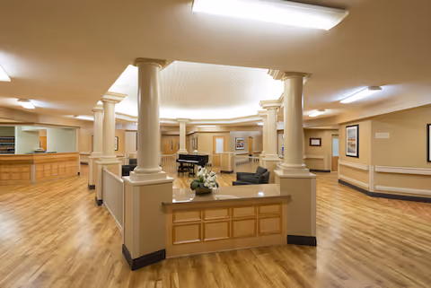 Senior living facility lobby with central reception, columns, seating areas, and a grand piano.