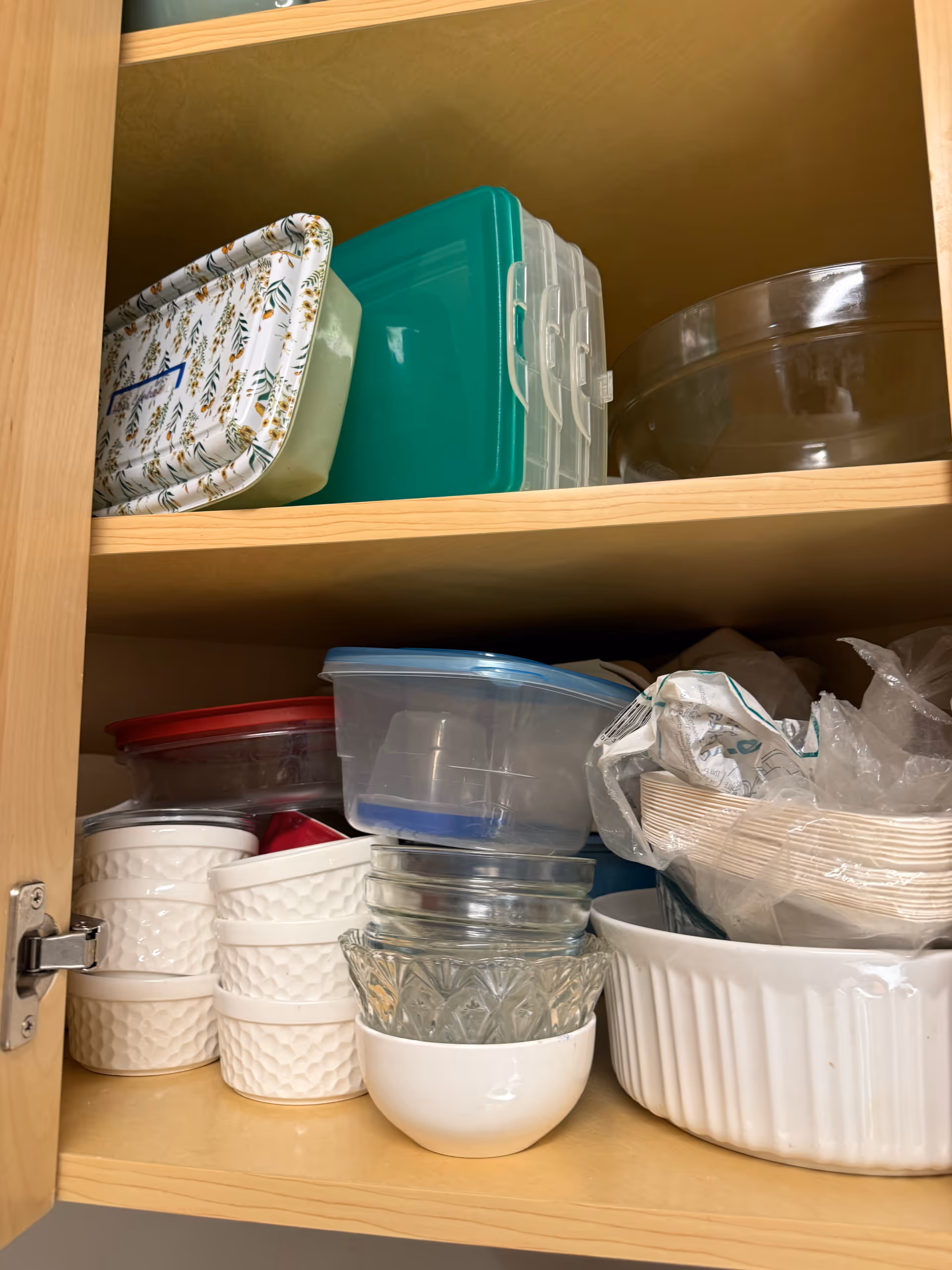 Open cabinet shelf filled with stacked bowls, glassware, and plastic containers.