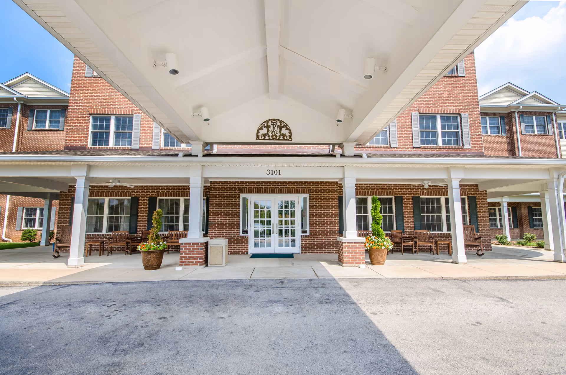 Brick senior living facility entrance with a covered drop-off area and seating.