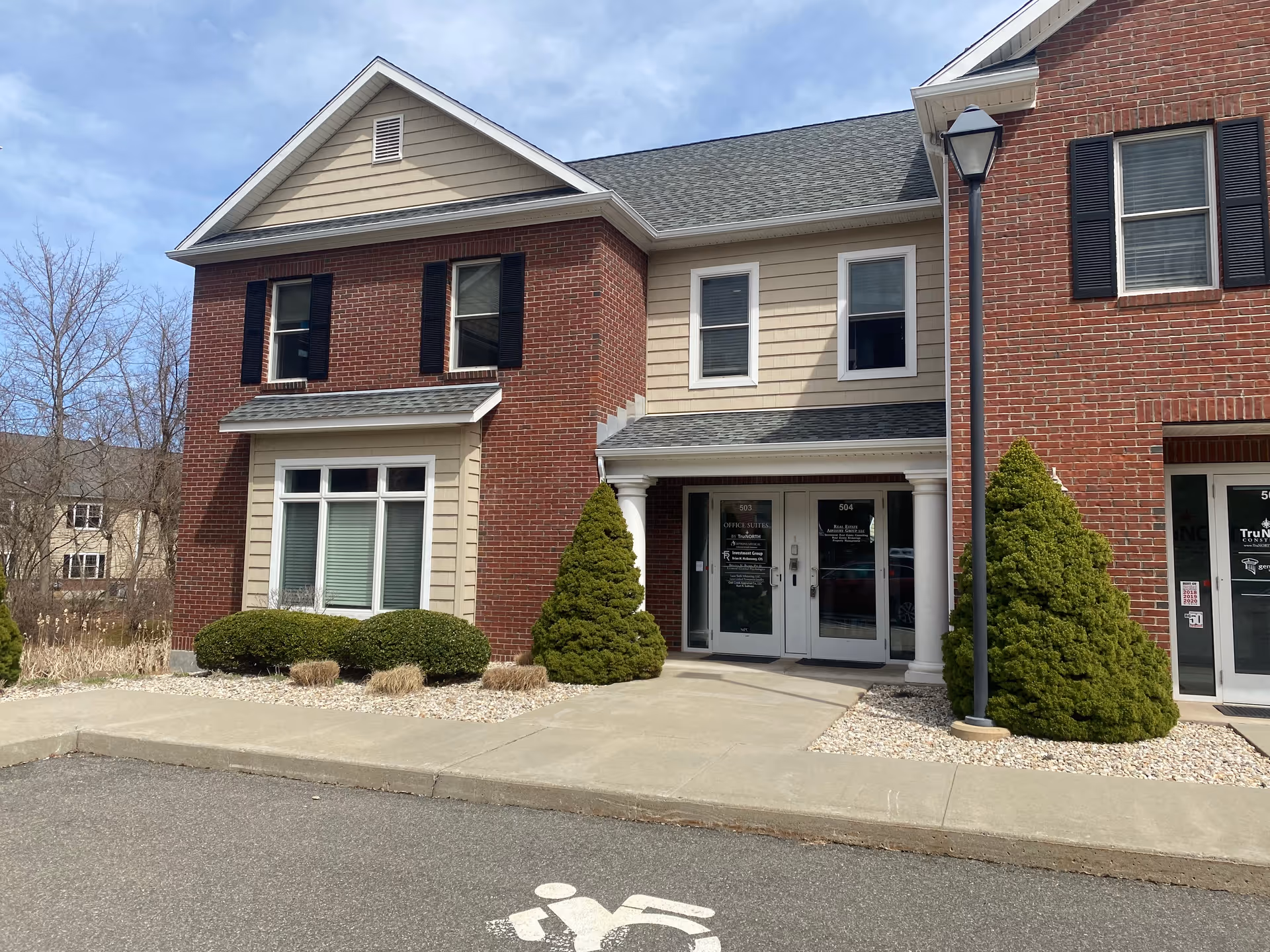 Exterior view of a two-story building with brick, beige siding, glass doors, and landscaping.