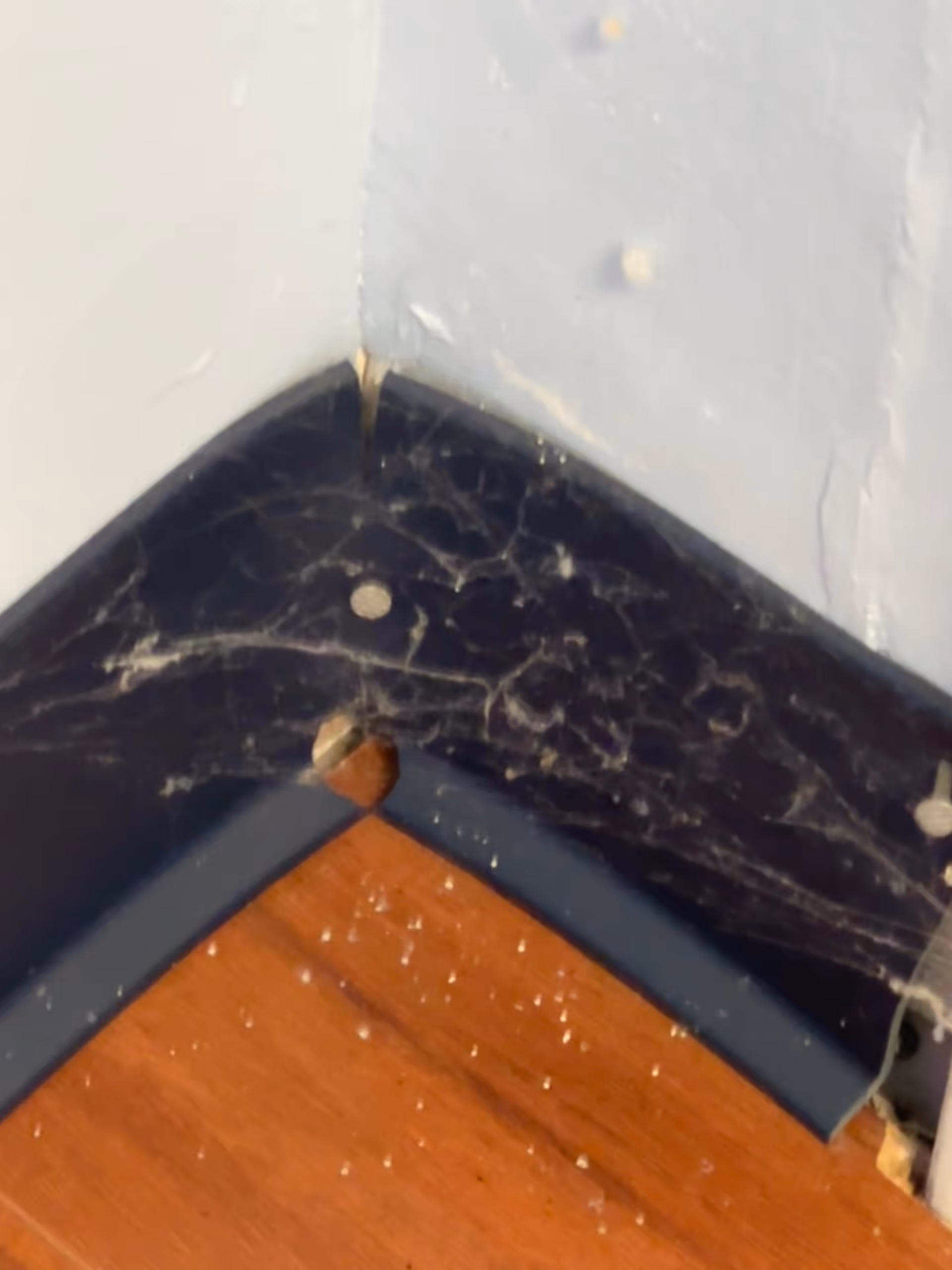 Close-up of a damaged interior corner with blue wall, black marble trim, and wooden floor.