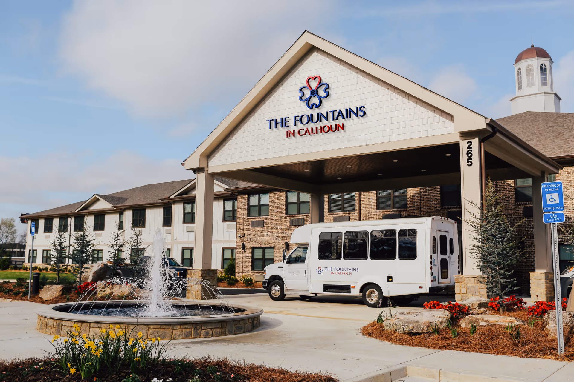 Front view of The Fountains in Calhoun with entrance, fountain, and a parked bus.