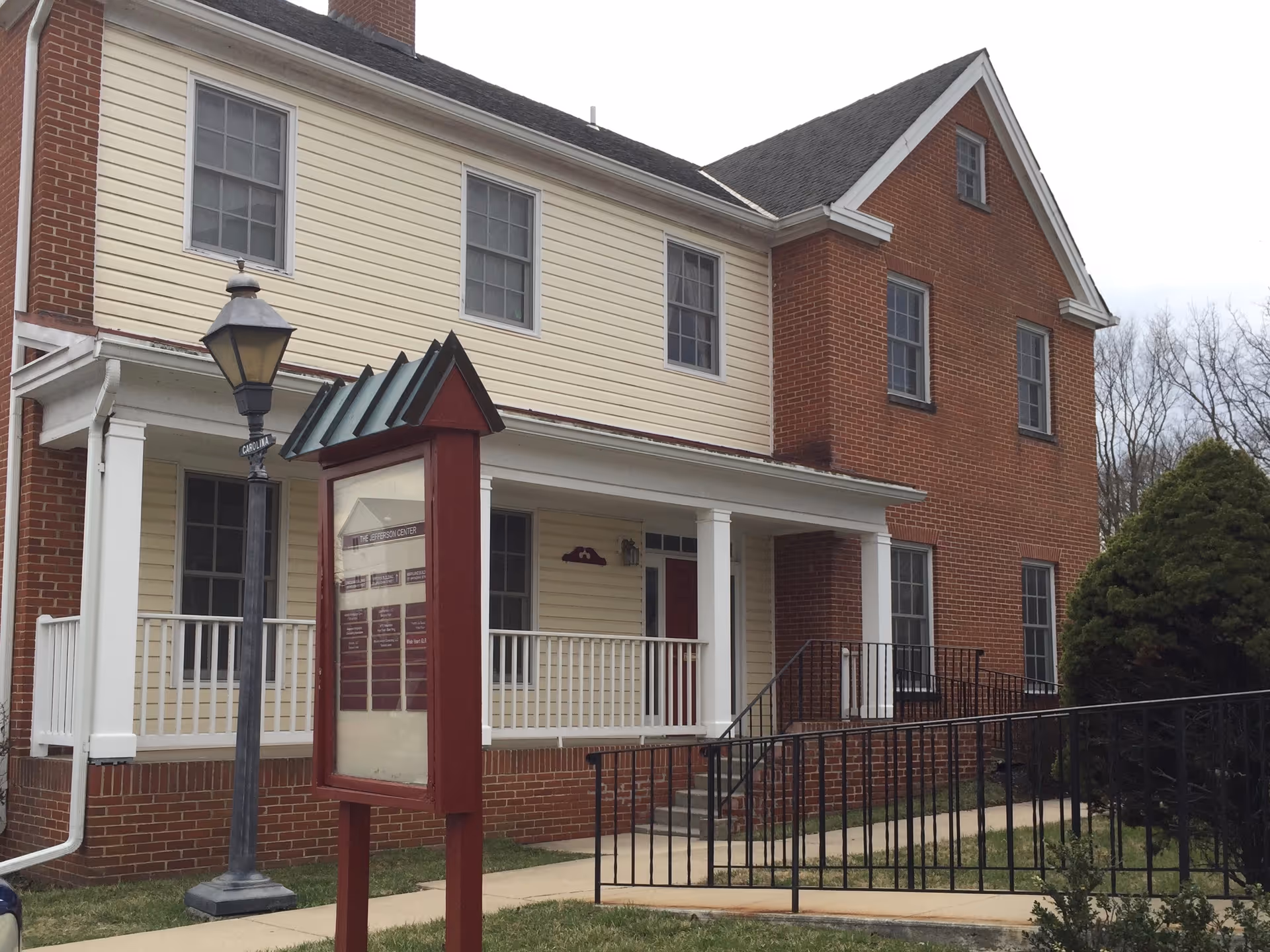 Two-story building with beige siding and brick facade, front porch, and informational sign.