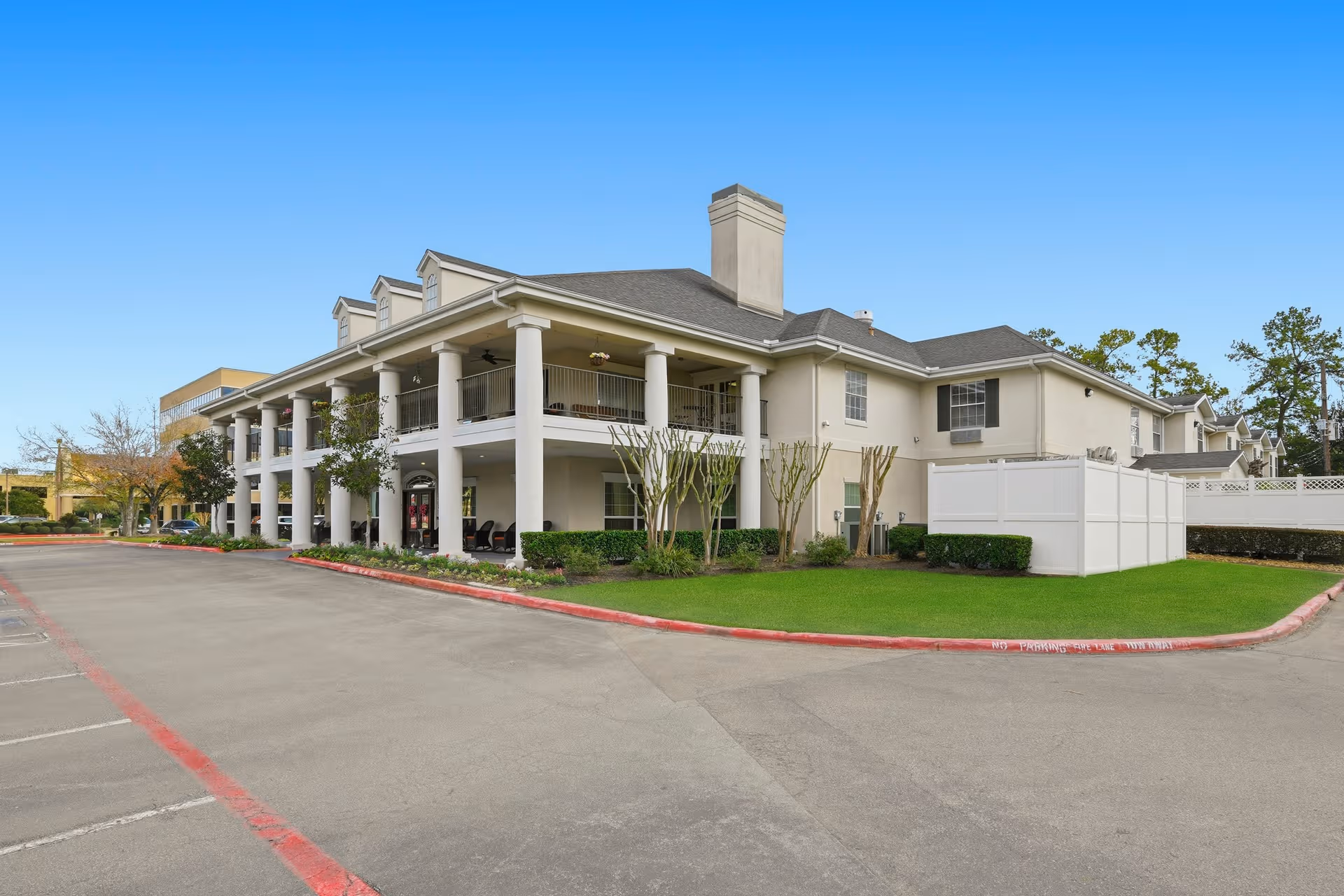 Cream-colored senior living building with tall white columns, two-story porch, and manicured lawn.
