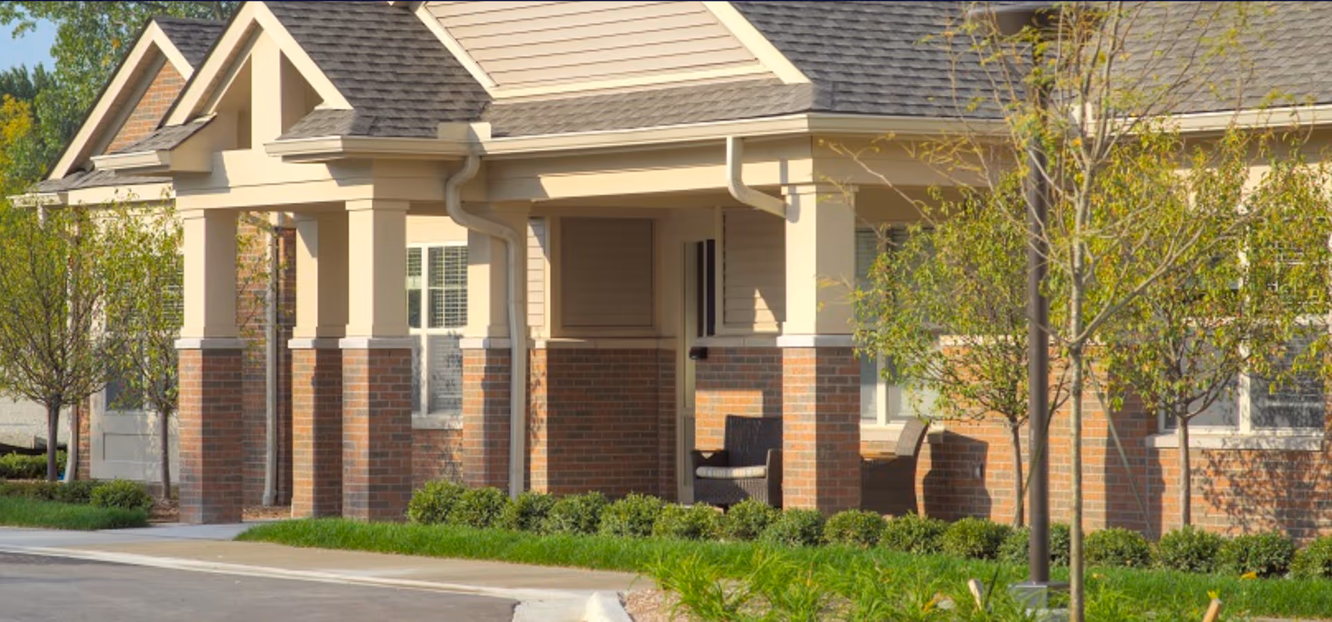Exterior view of an American House Freedom Place Rochester entrance with brick columns and landscaping.