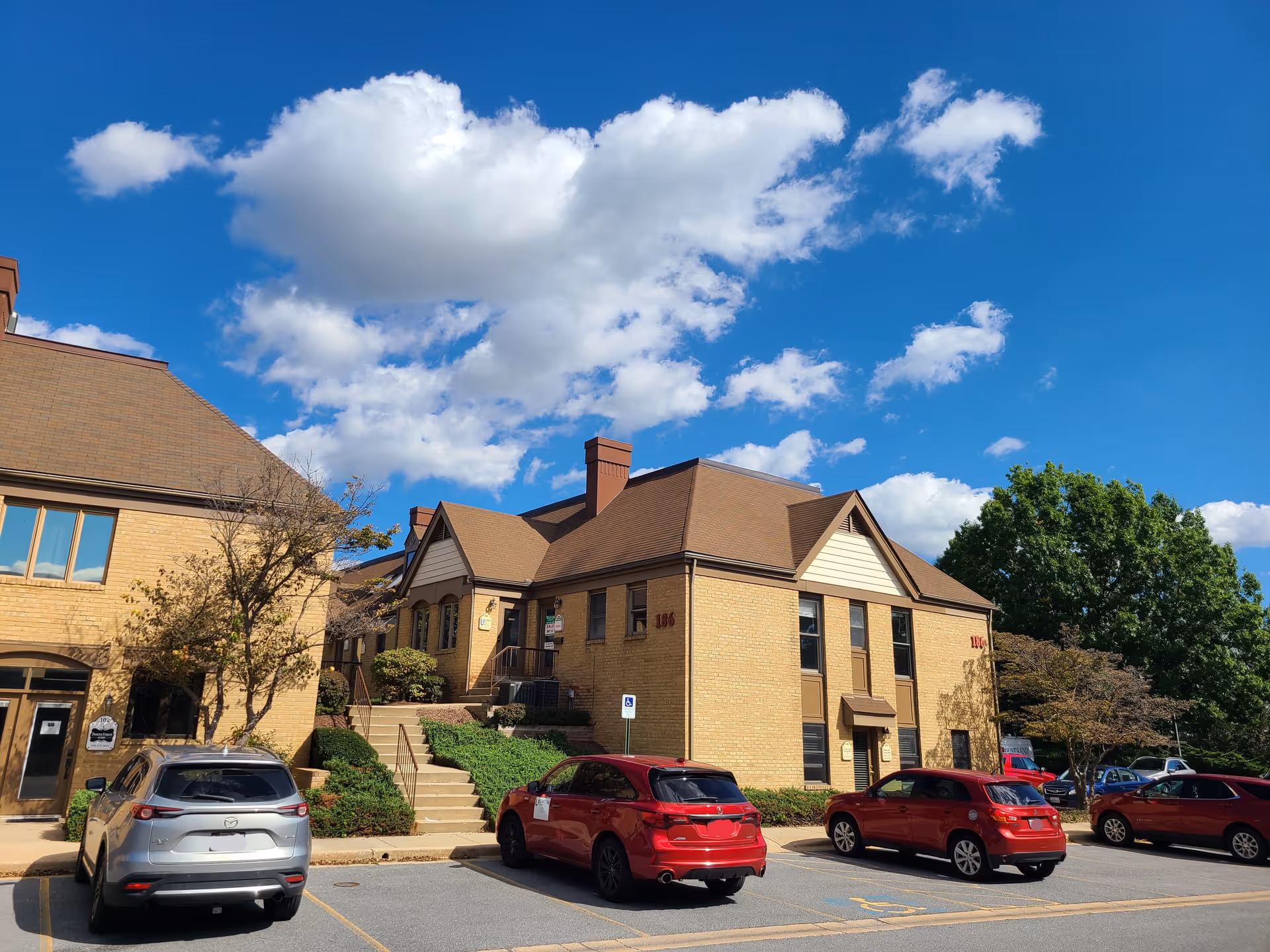Brick senior living facility exterior with an entrance, steps, and parked cars under blue sky.