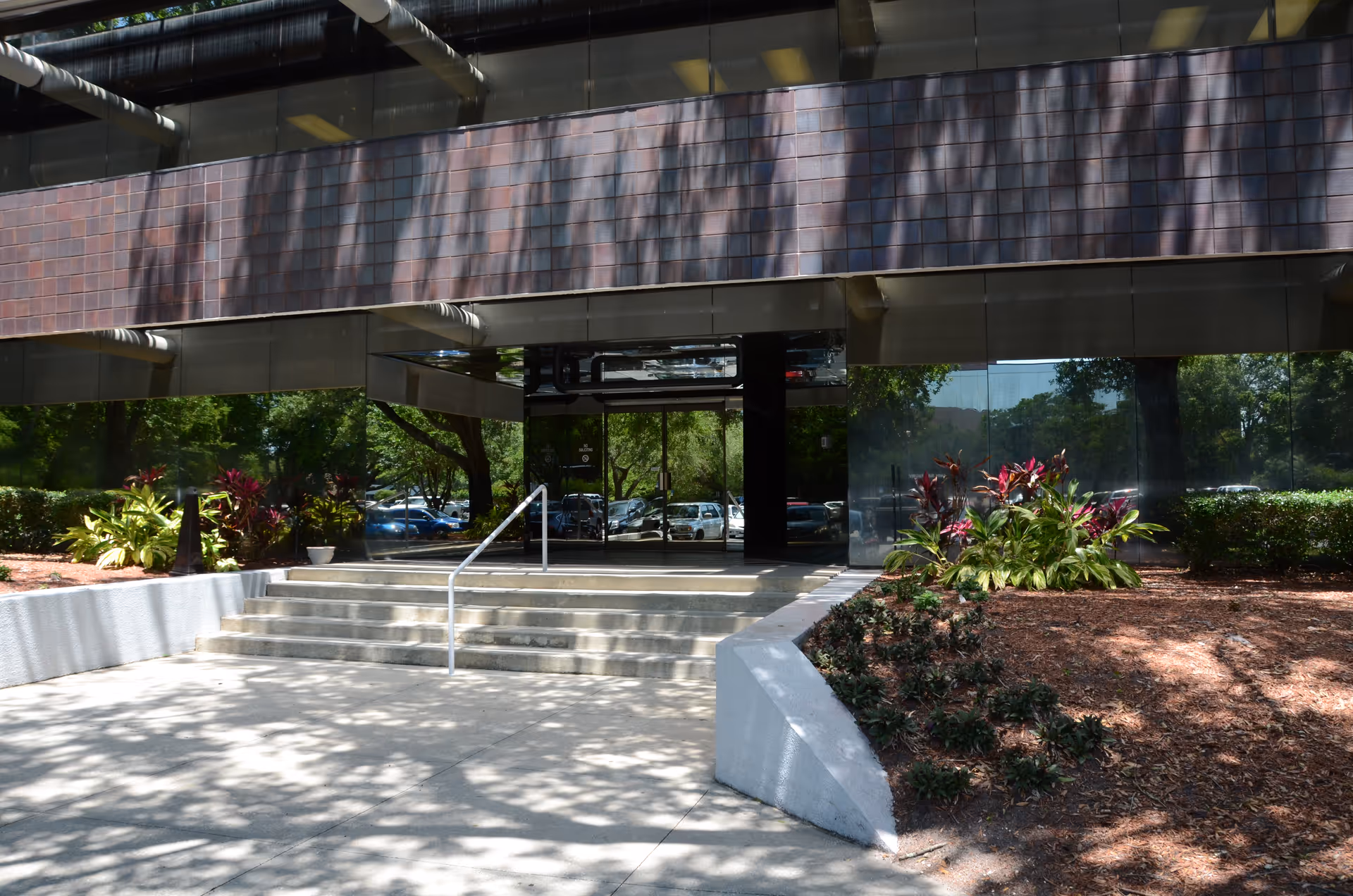 Modern building entrance with glass doors, stairs, and landscaped front garden.