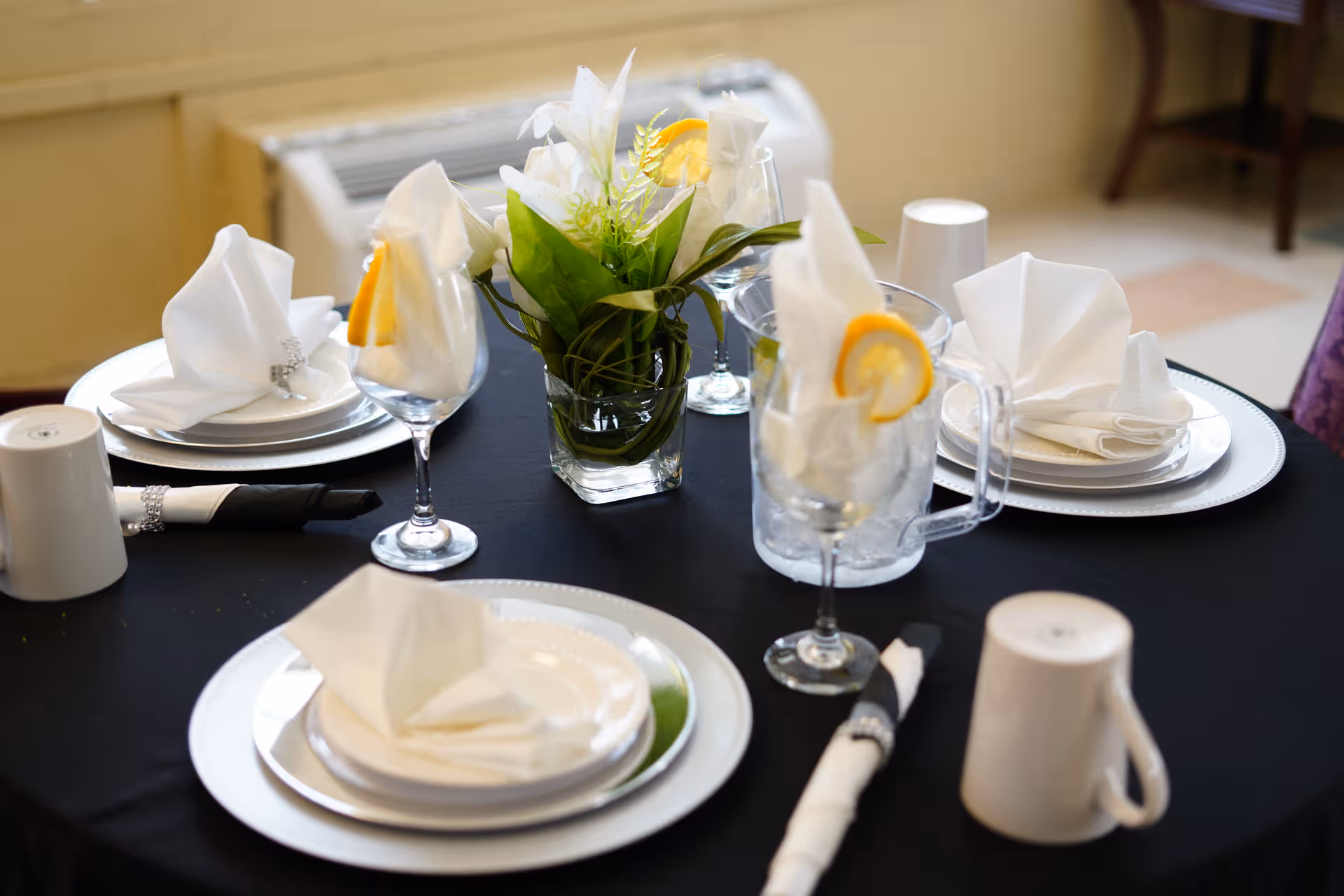 Table set for a formal meal with folded napkins, glassware, and a floral centerpiece.