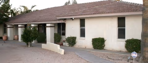 Single-story beige senior living facility exterior with a red-tiled roof and shrubs.
