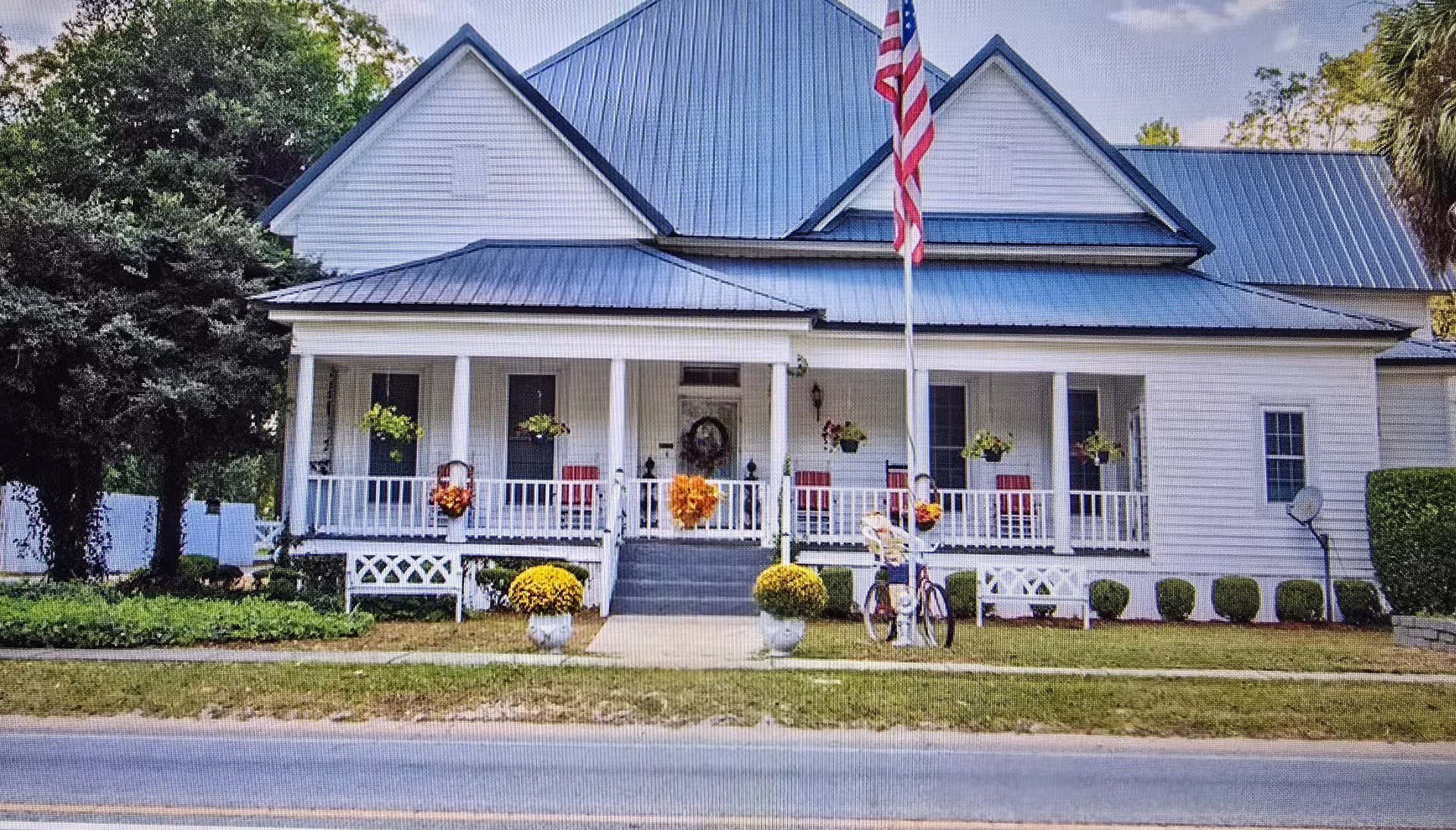 White front porch of a senior living home with chairs, plants, and an American flag.