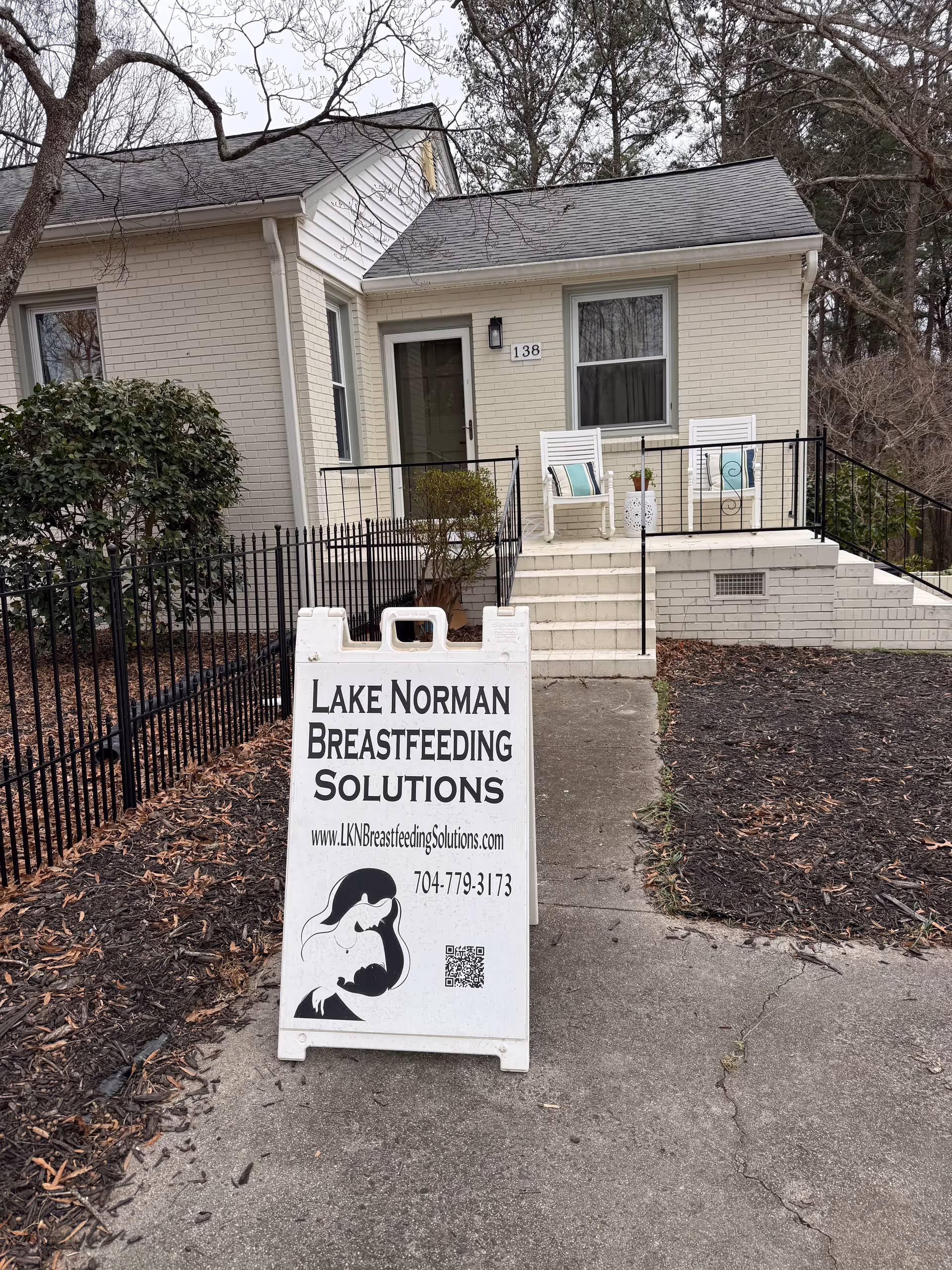 Exterior view of a small brick building with steps, railing, and Lake Norman Breastfeeding Solutions sign.