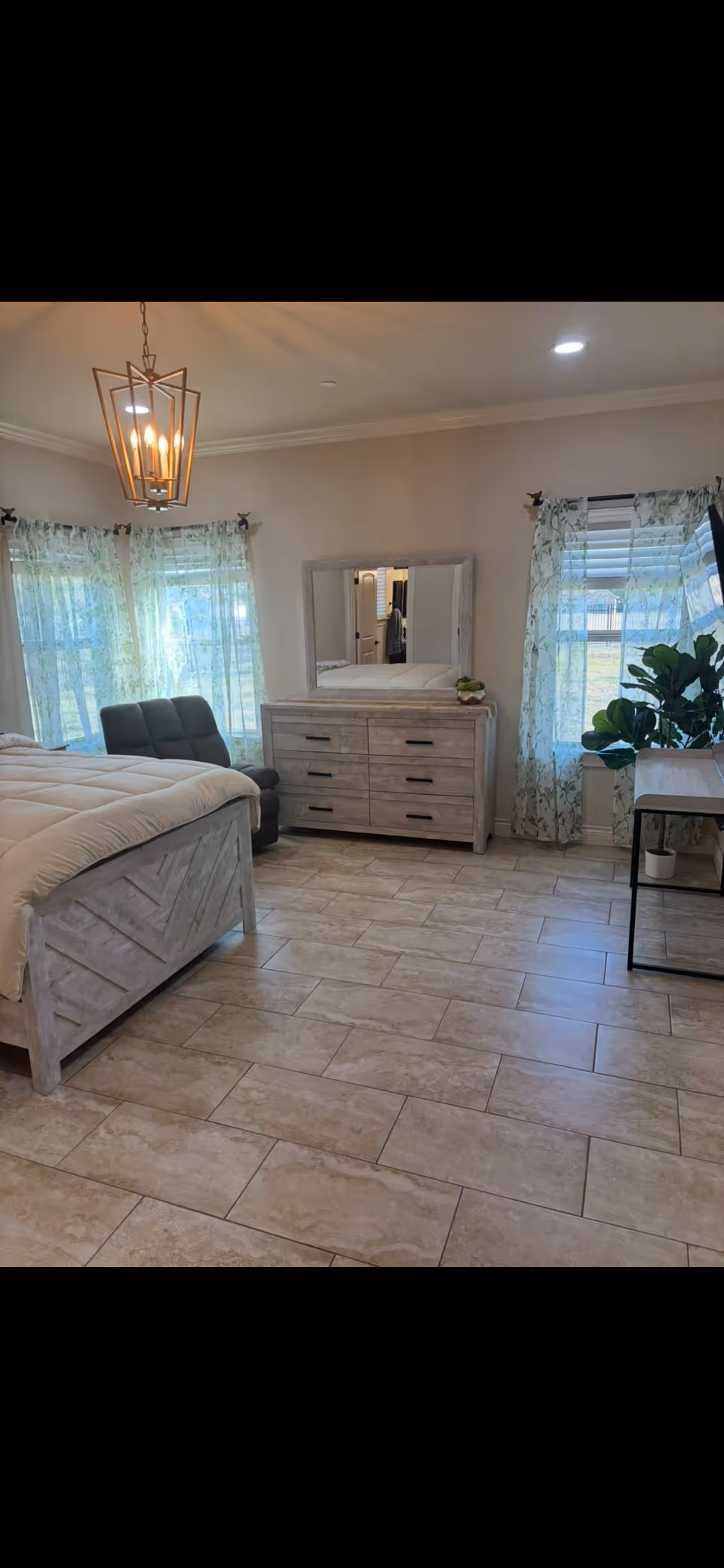 Bright bedroom in a senior living facility with bed, dresser, mirror, and plants.