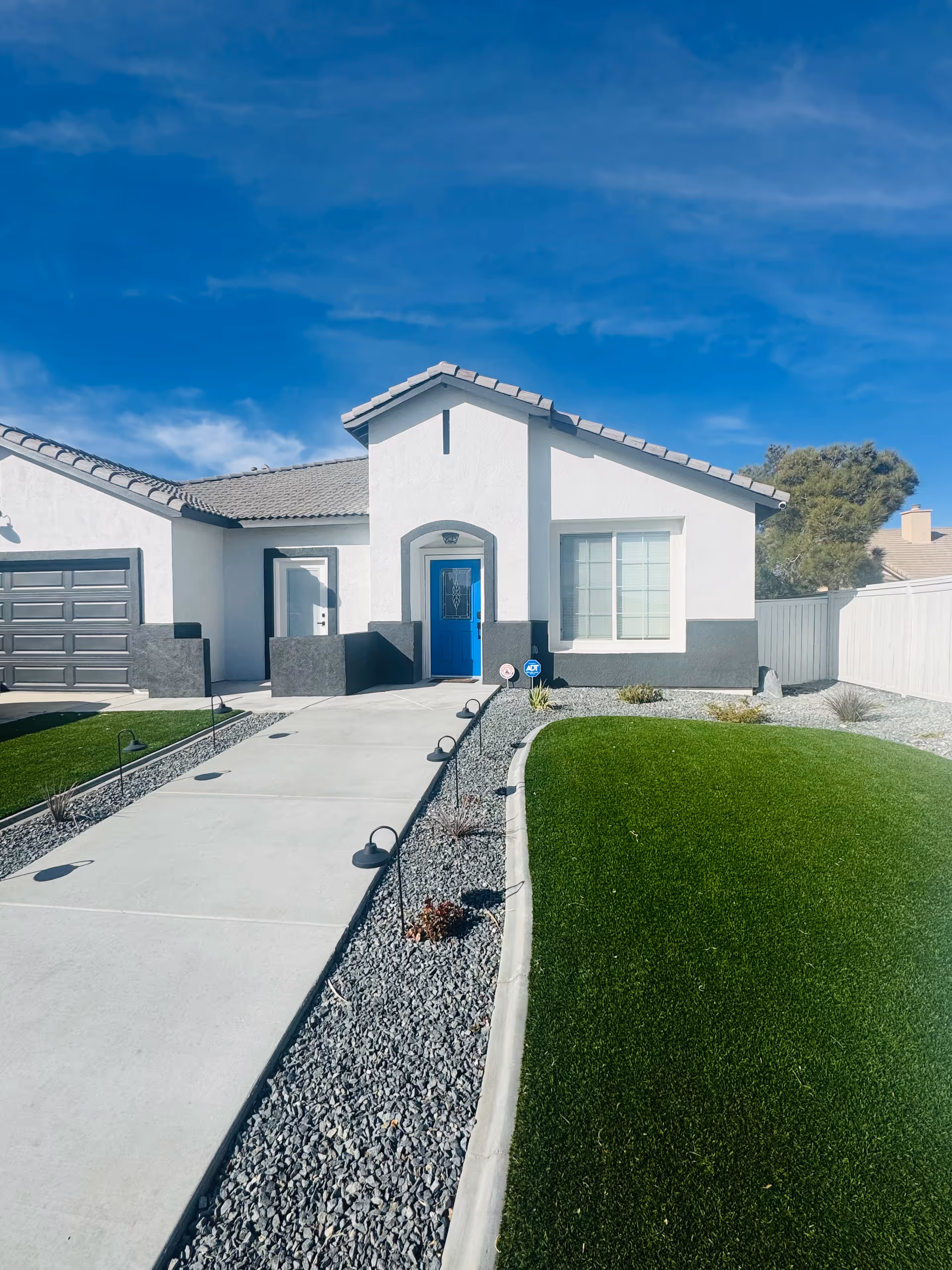 White modern single-story building facade with blue front door and landscaped pathway.