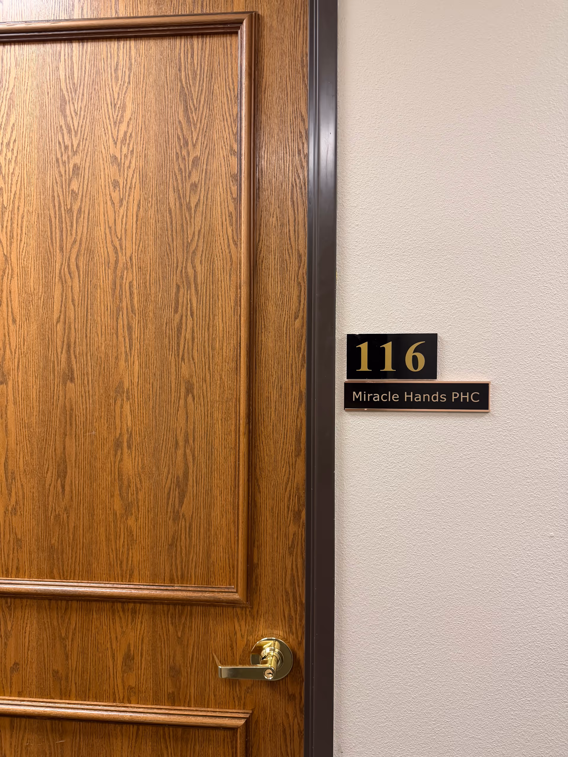 Wooden interior door labeled room 116 with Miracle Hands PHC plaque