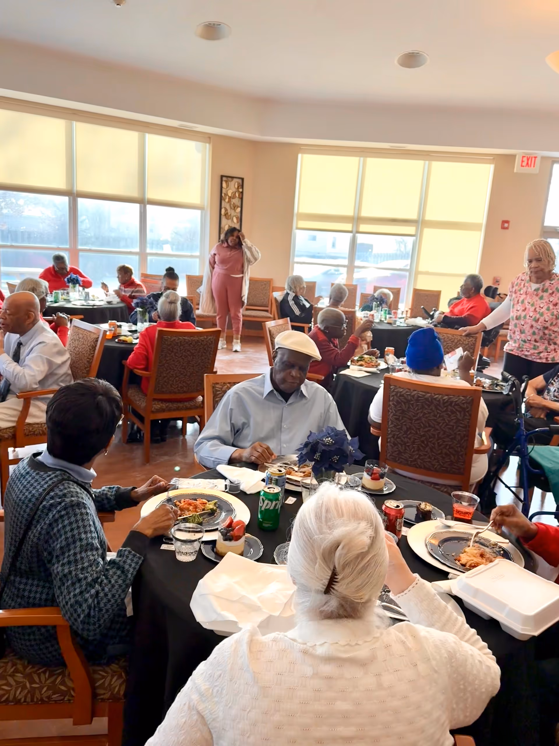 Residents enjoy meals in a bright Harmony House Cares dining hall with round tables.