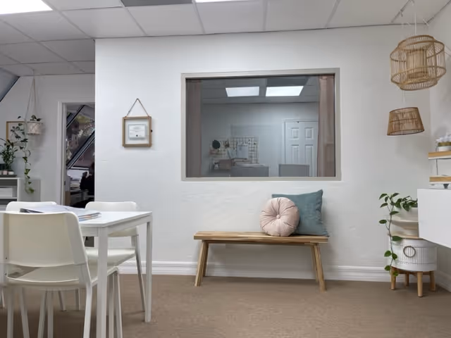 Interior common area with white walls, bench, cushions, dining table, and plants.