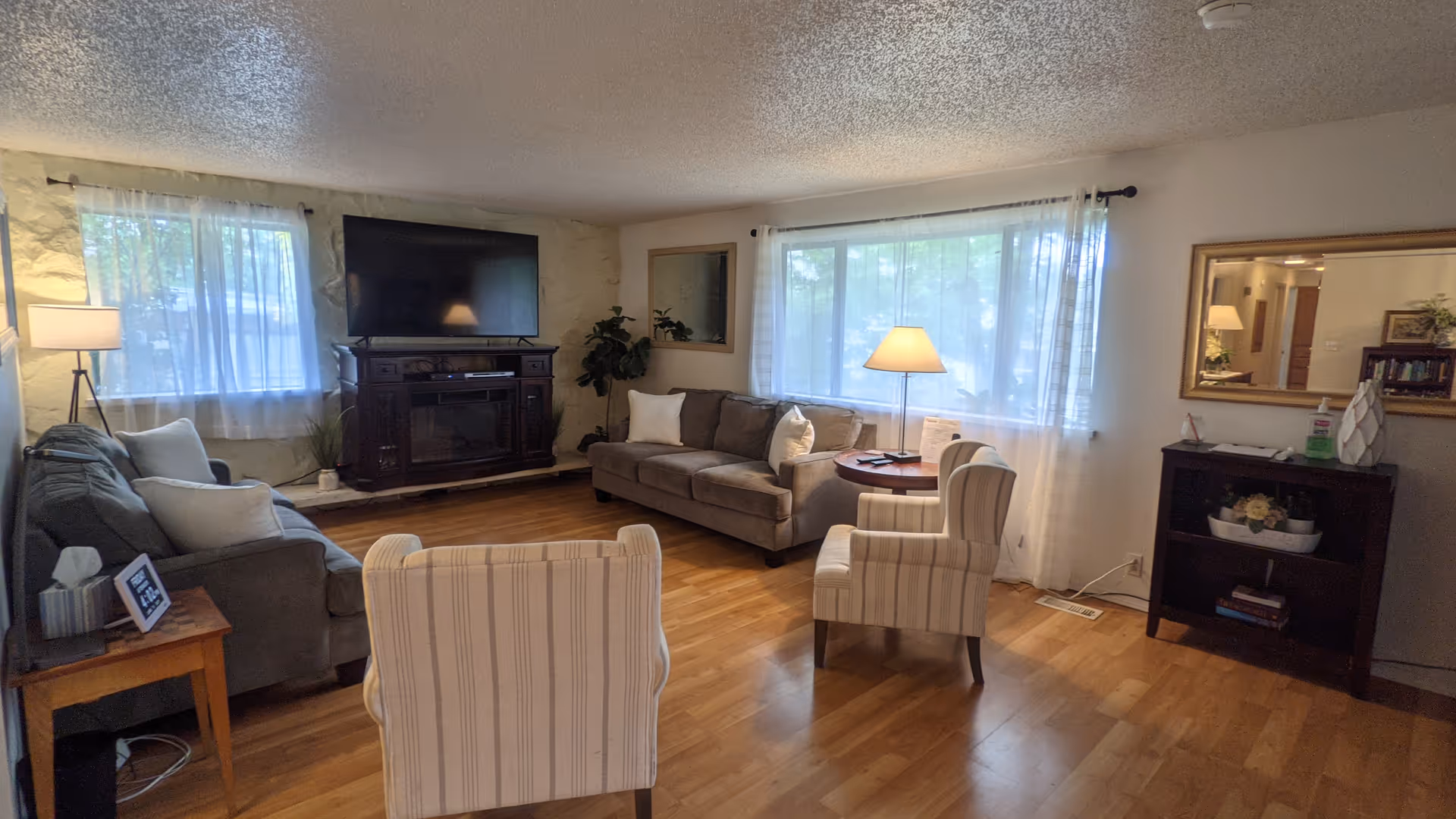 Cozy living room with sofa, chairs, TV, and large windows.