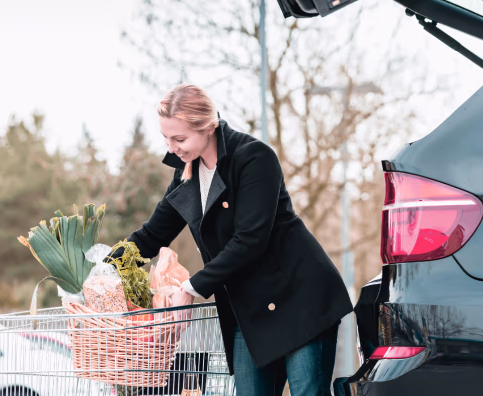 Woman loading groceries from car into shopping cart outdoors.