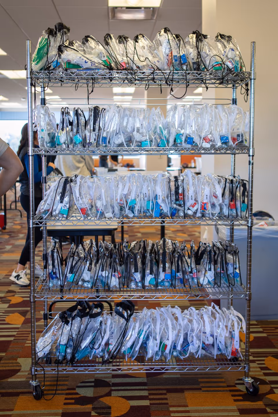 Metal rolling rack stocked with clear plastic bags containing assorted items, located in an interior facility.