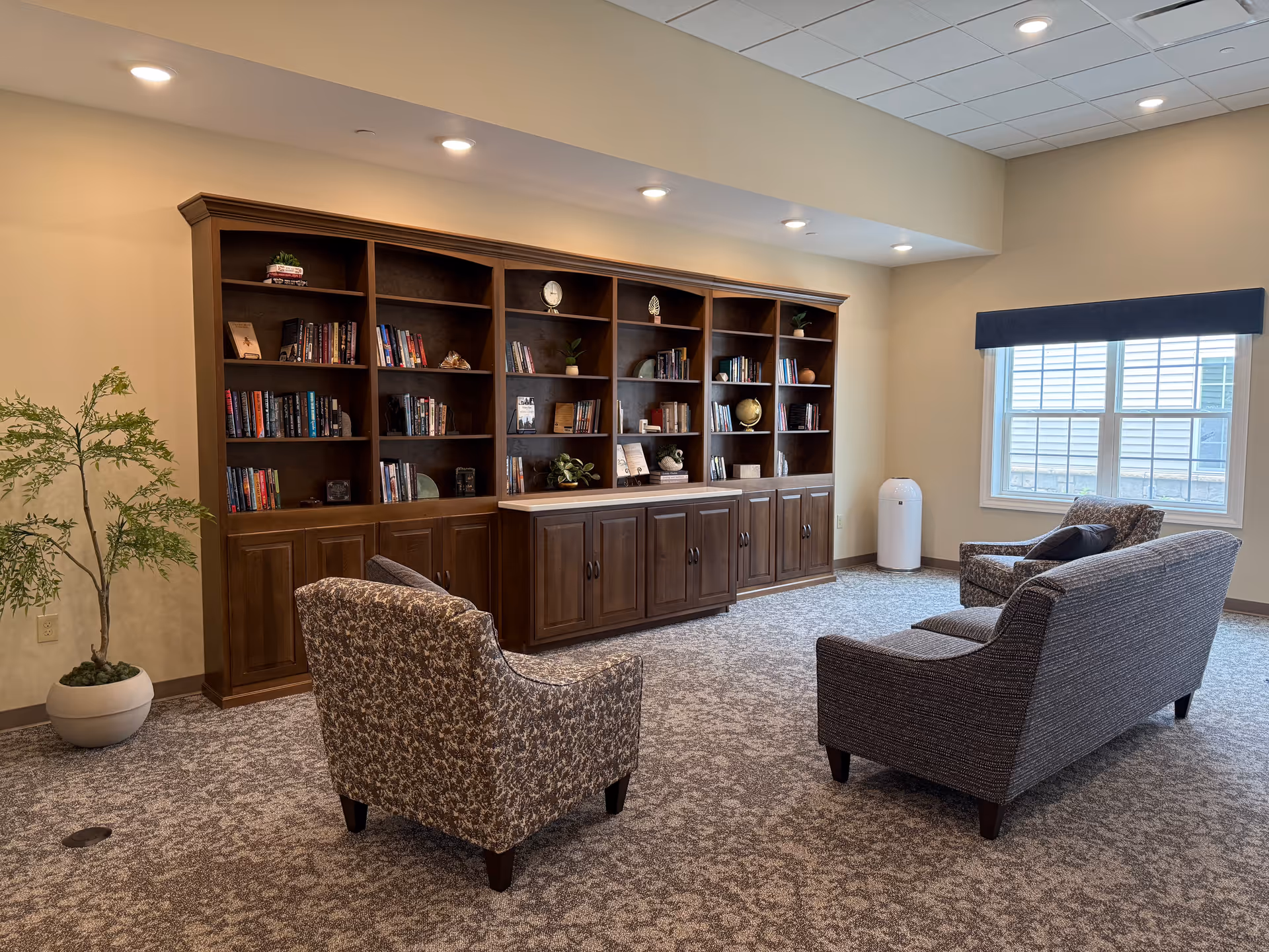 A cozy lounge area with a large wooden bookshelf, armchairs, and a window