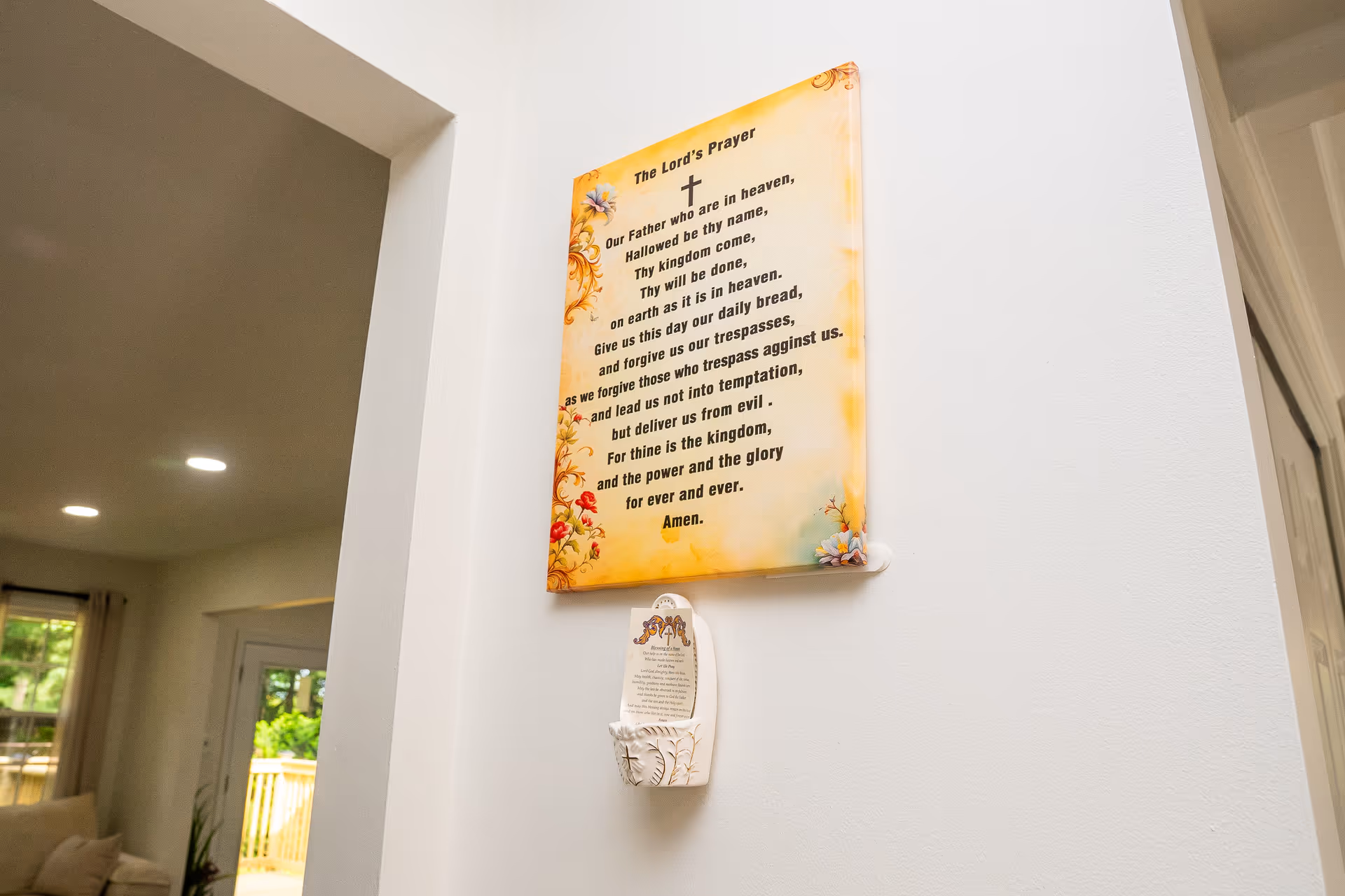 Interior hallway with a religious plaque on a white wall and living area visible.
