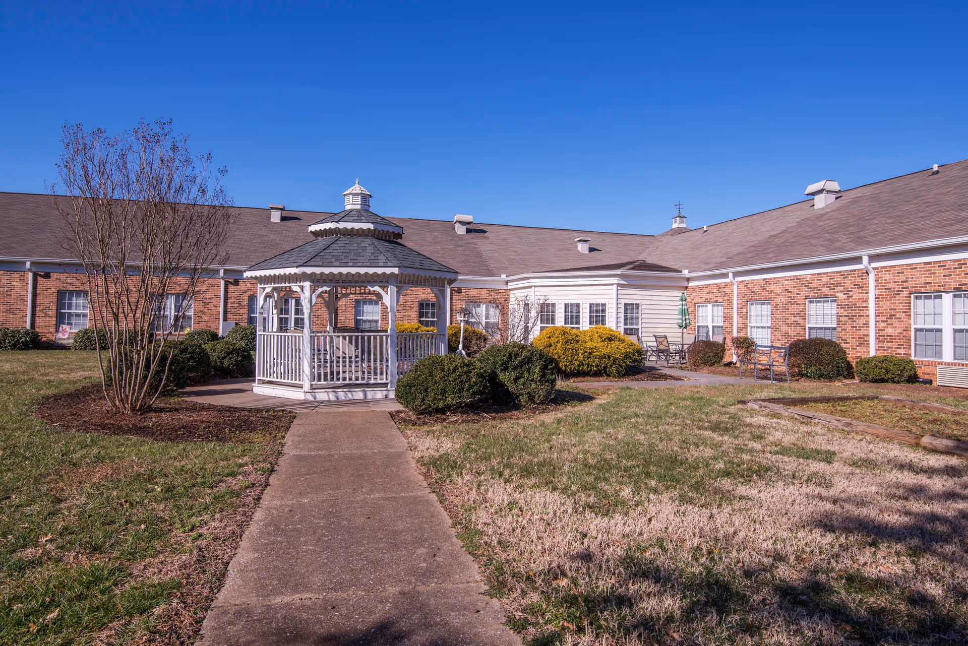 Brick senior living facility with a white gazebo, path, and shrubs outside