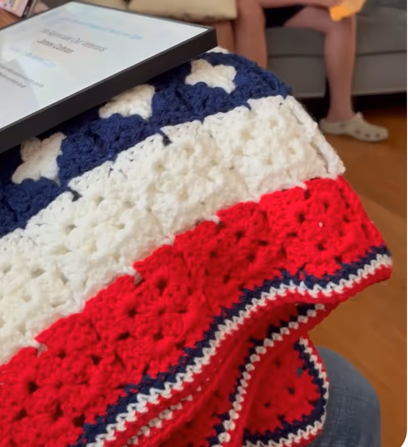 A crocheted red, white, and blue blanket draped over a lap indoors.