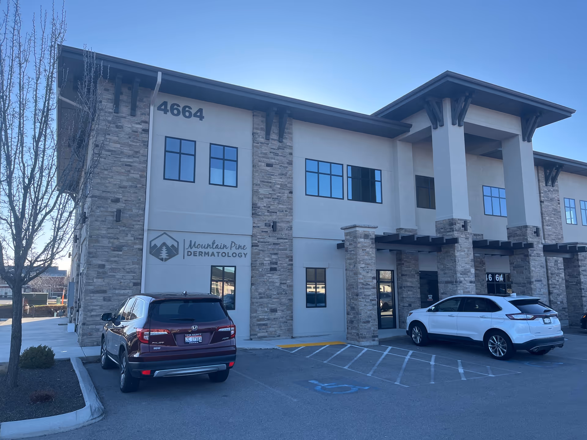 Two-story medical building with stone pillars and parked cars in front.