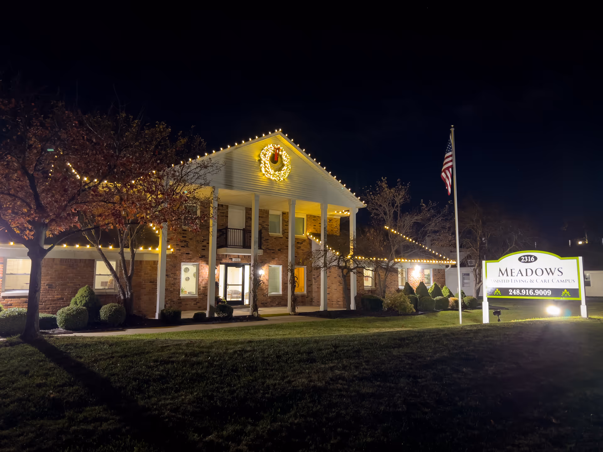 Night exterior view of Meadows of Troy facility with festive lights and a front sign