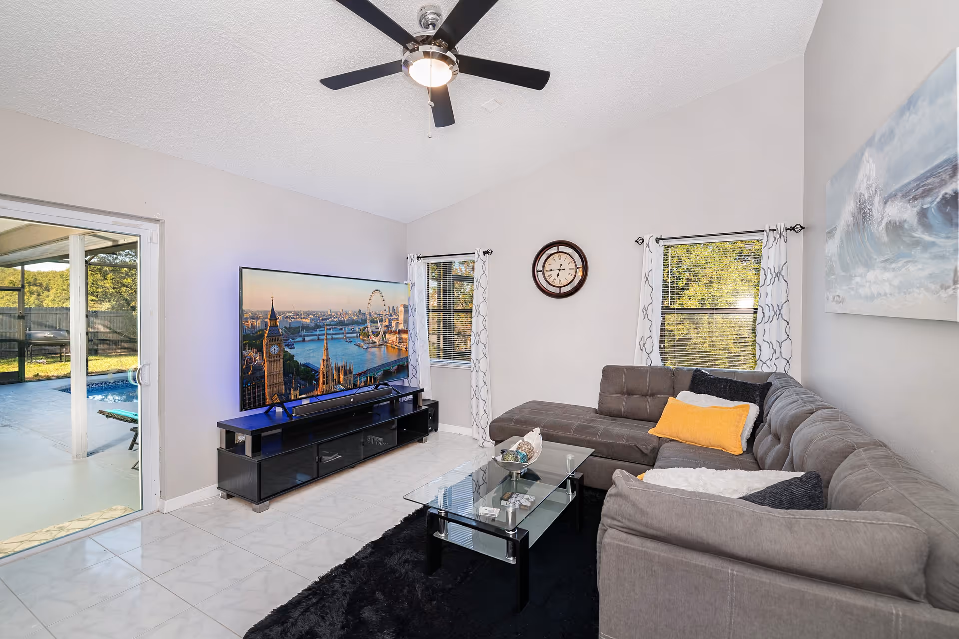 Bright living room with gray sectional sofa, glass coffee table, TV, and ceiling fan.