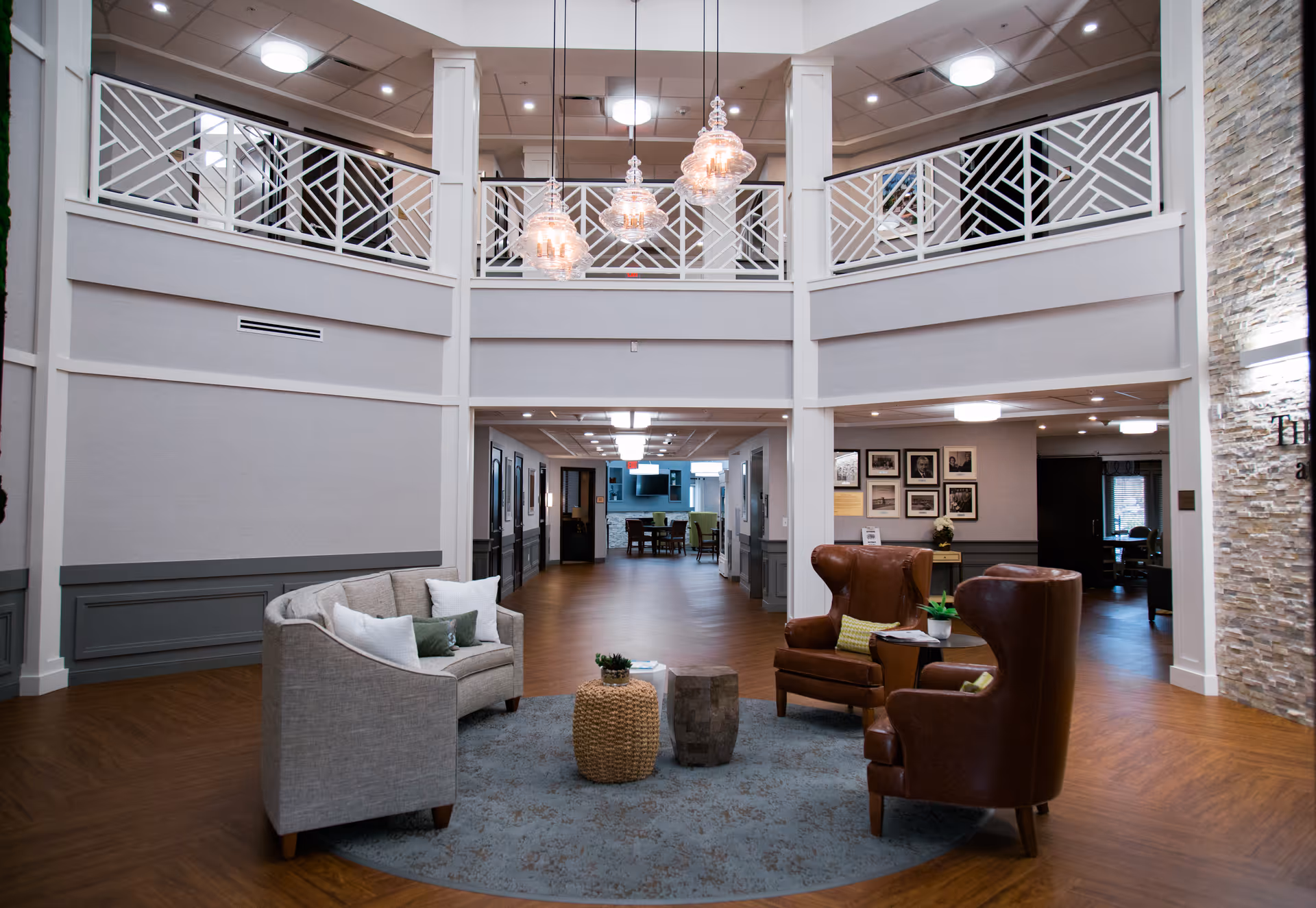 Bright two-level lobby with seating, chandeliers, and a central rug in a senior living facility.