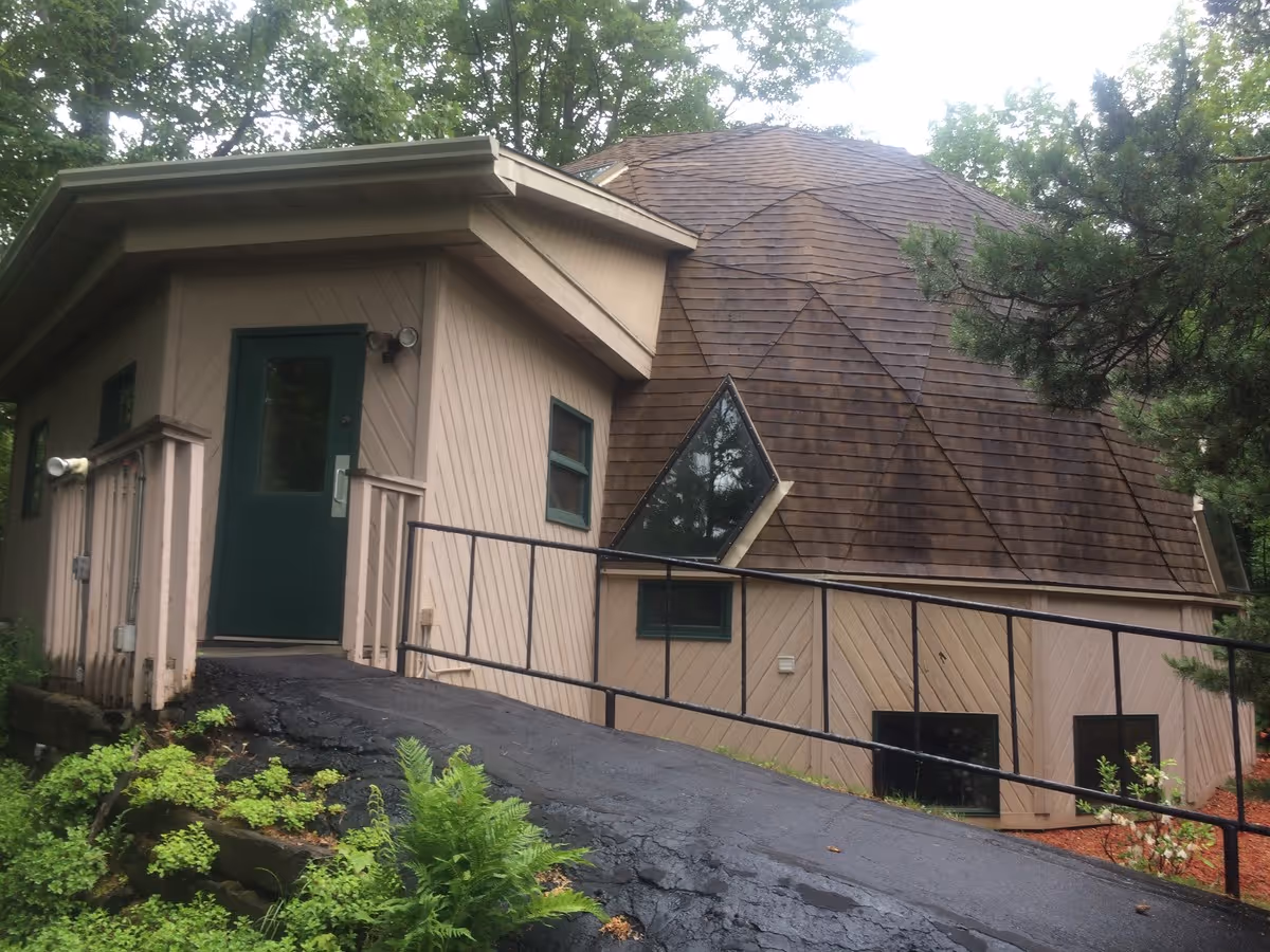 Exterior view of a beige building with green doors and a sloped wooden roof.