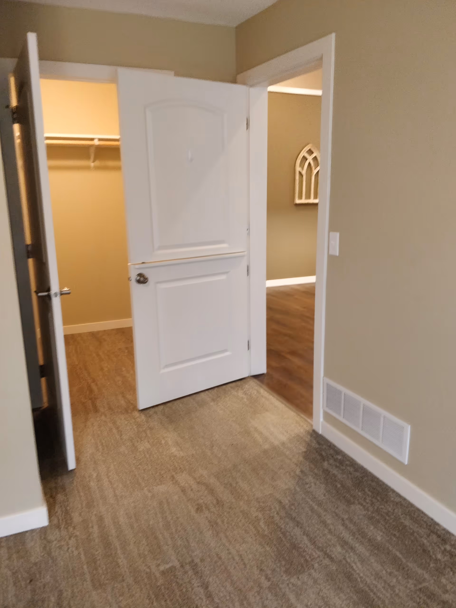 Beige-walled hallway with carpet and open doors to a closet and adjacent room.