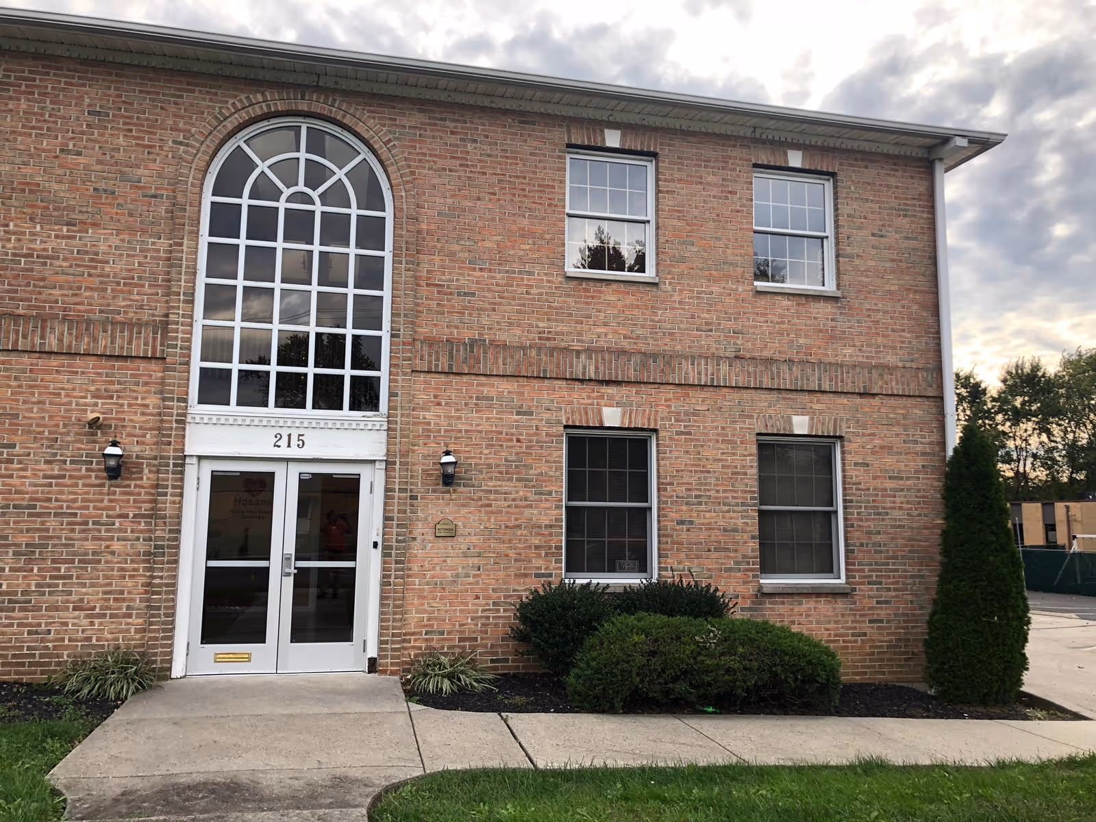 Two-story brick building with a large arched window above glass double doors.