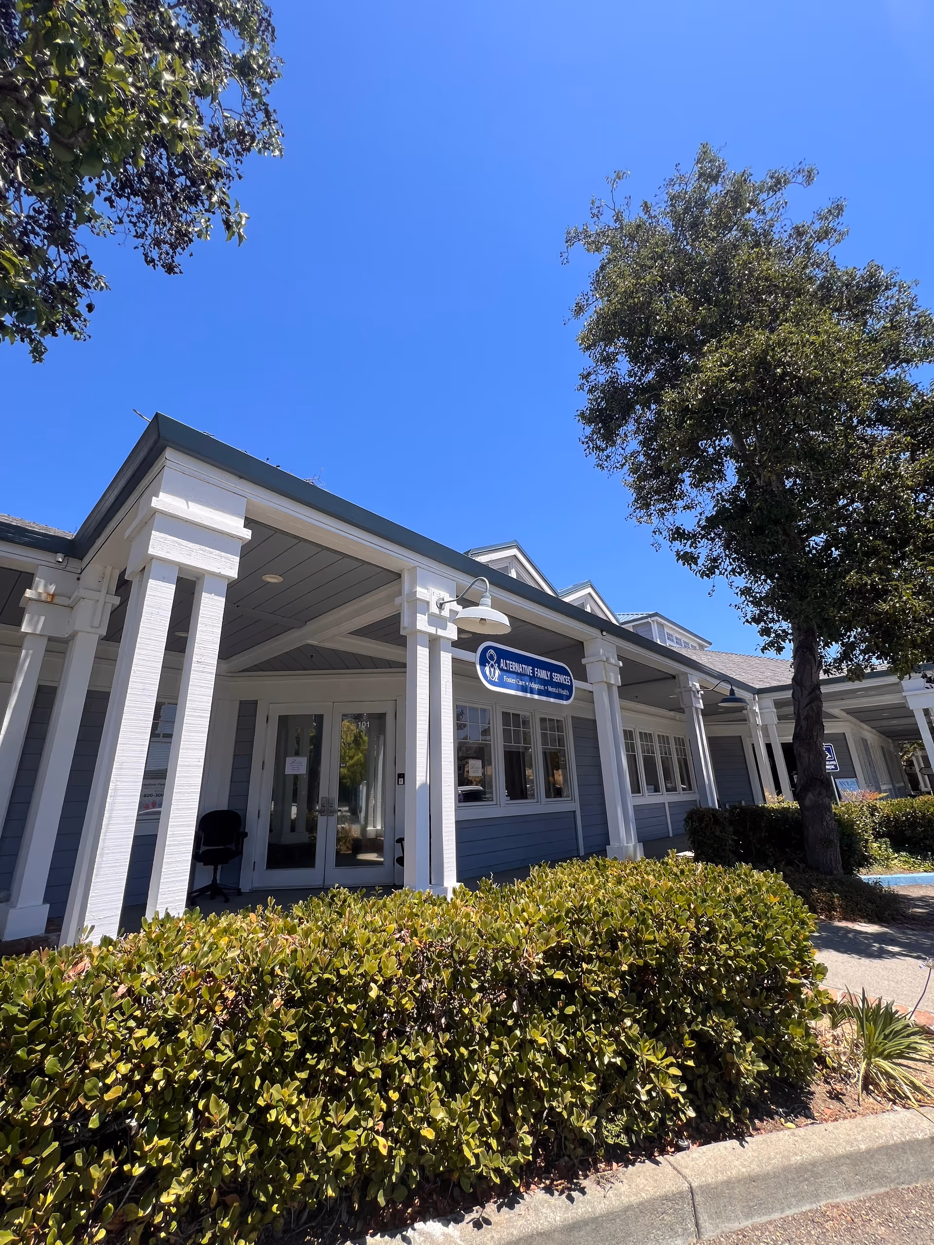 Exterior view of a light blue building with white columns and a sign.