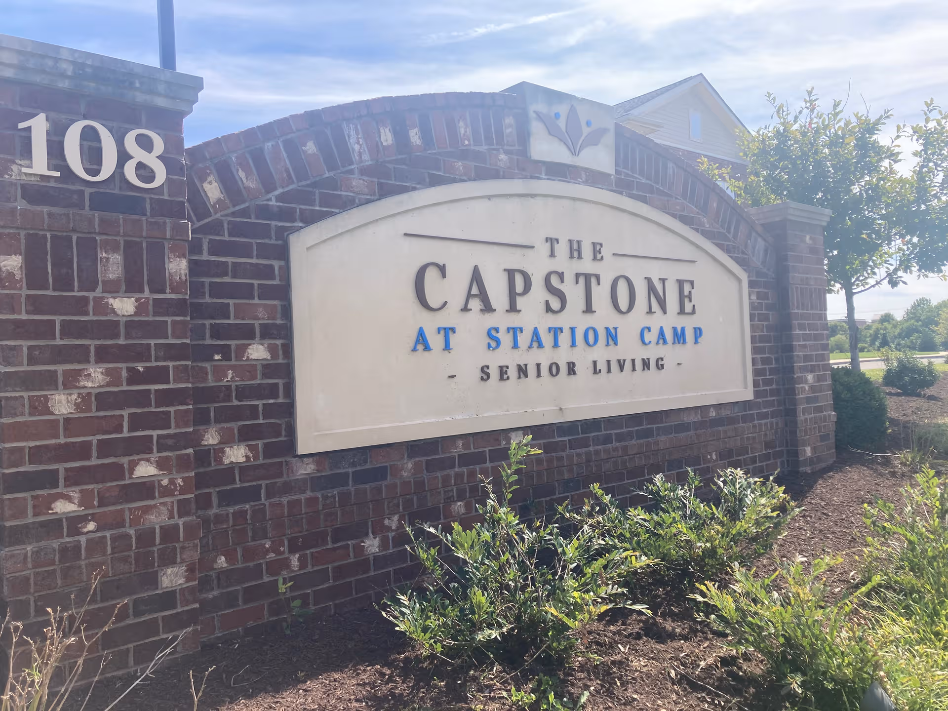 Brick sign reads The Capstone at Station Camp Senior Living with landscaping in front.