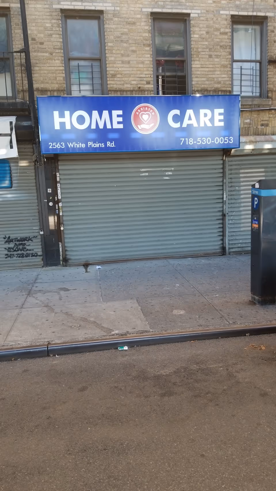 Blue sign reading HOME CARE above a closed metal shutter on a brick building.