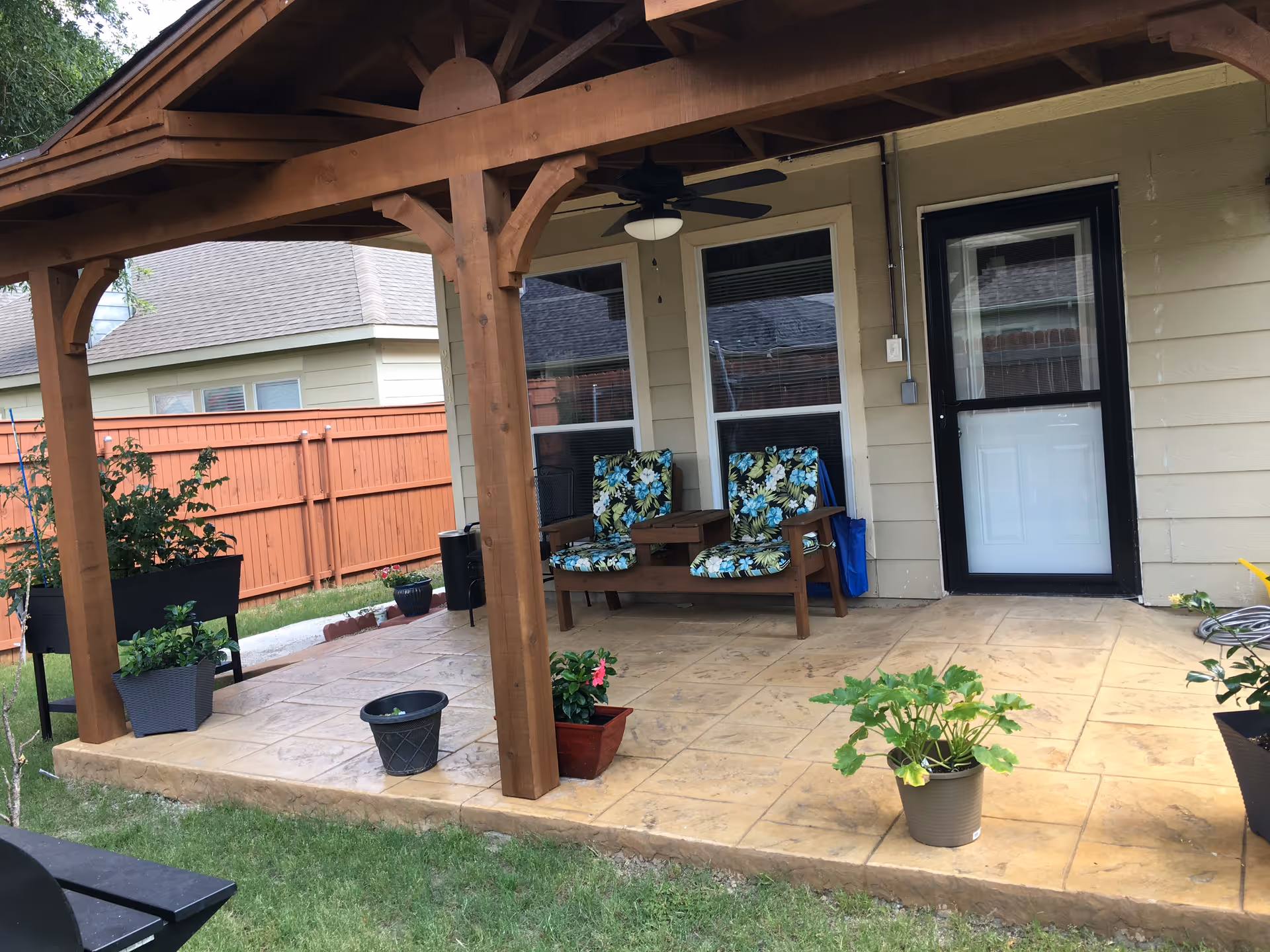 Covered patio with floral cushioned chairs, plants, and a back entrance.