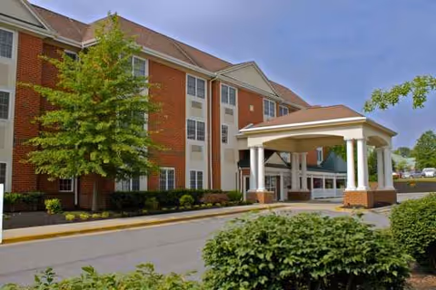 Arbor Terrace Senior Living exterior: brick building with a covered entrance and lush landscaping.
