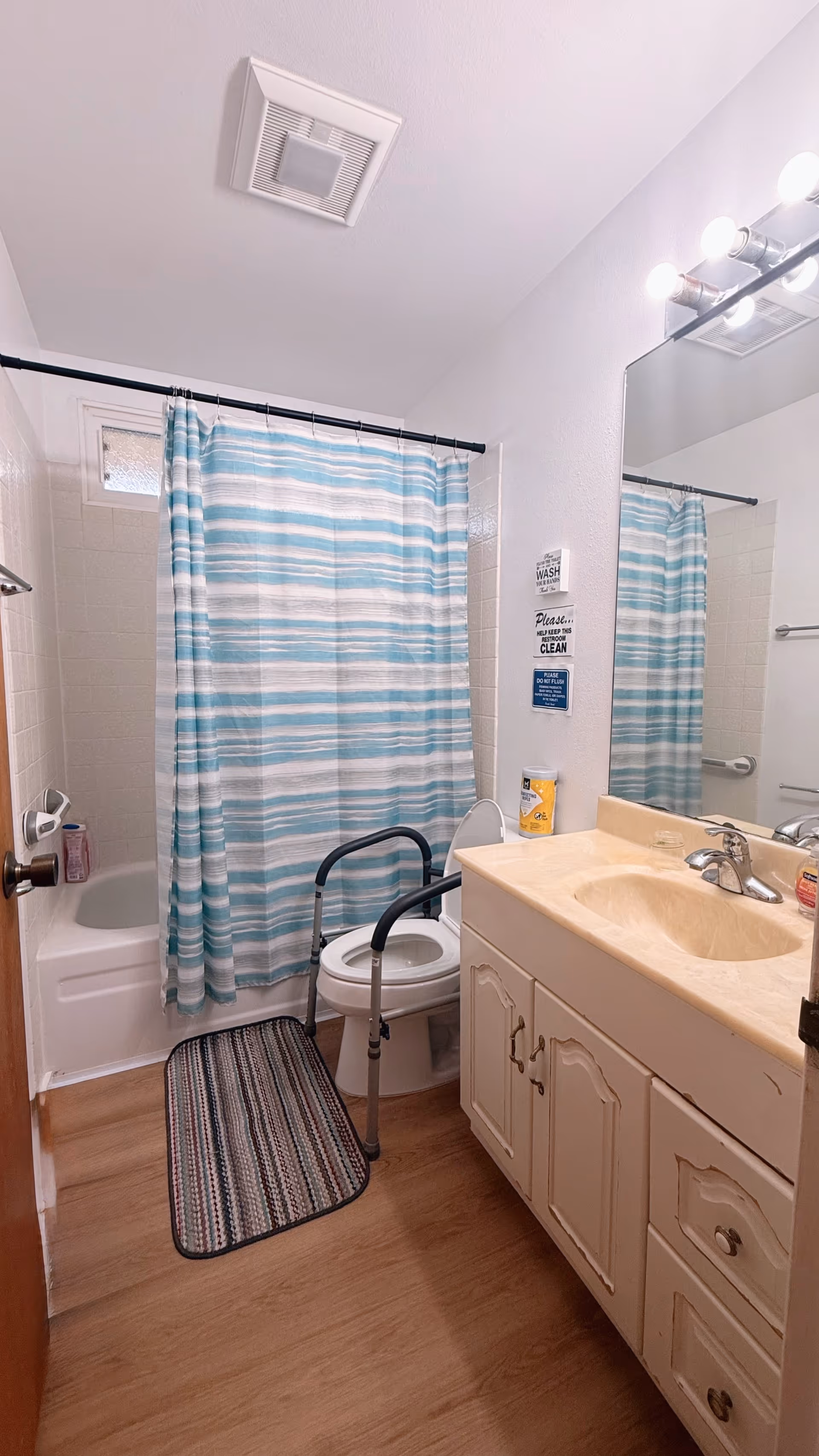 Small bathroom with striped shower curtain, sink, toilet, and mobility aid in a senior home.