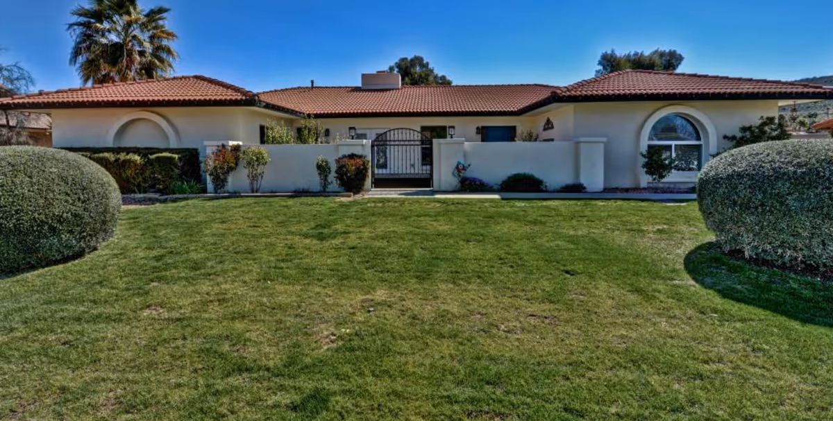 Front view of a single-story assisted living building with gate, lawn, and arched windows.