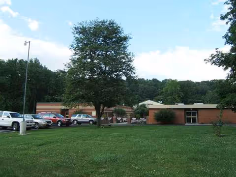 Exterior view of a brick nursing home with a parking lot and green lawn.