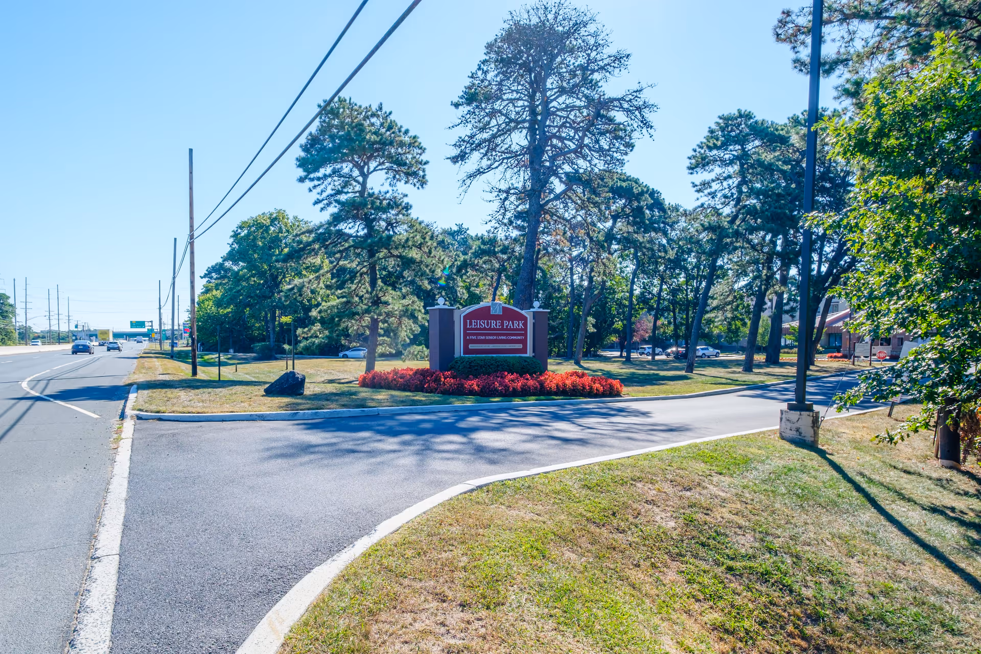 Entrance driveway and landscaped sign reading 'Leisure Park' surrounded by trees and a roadway.