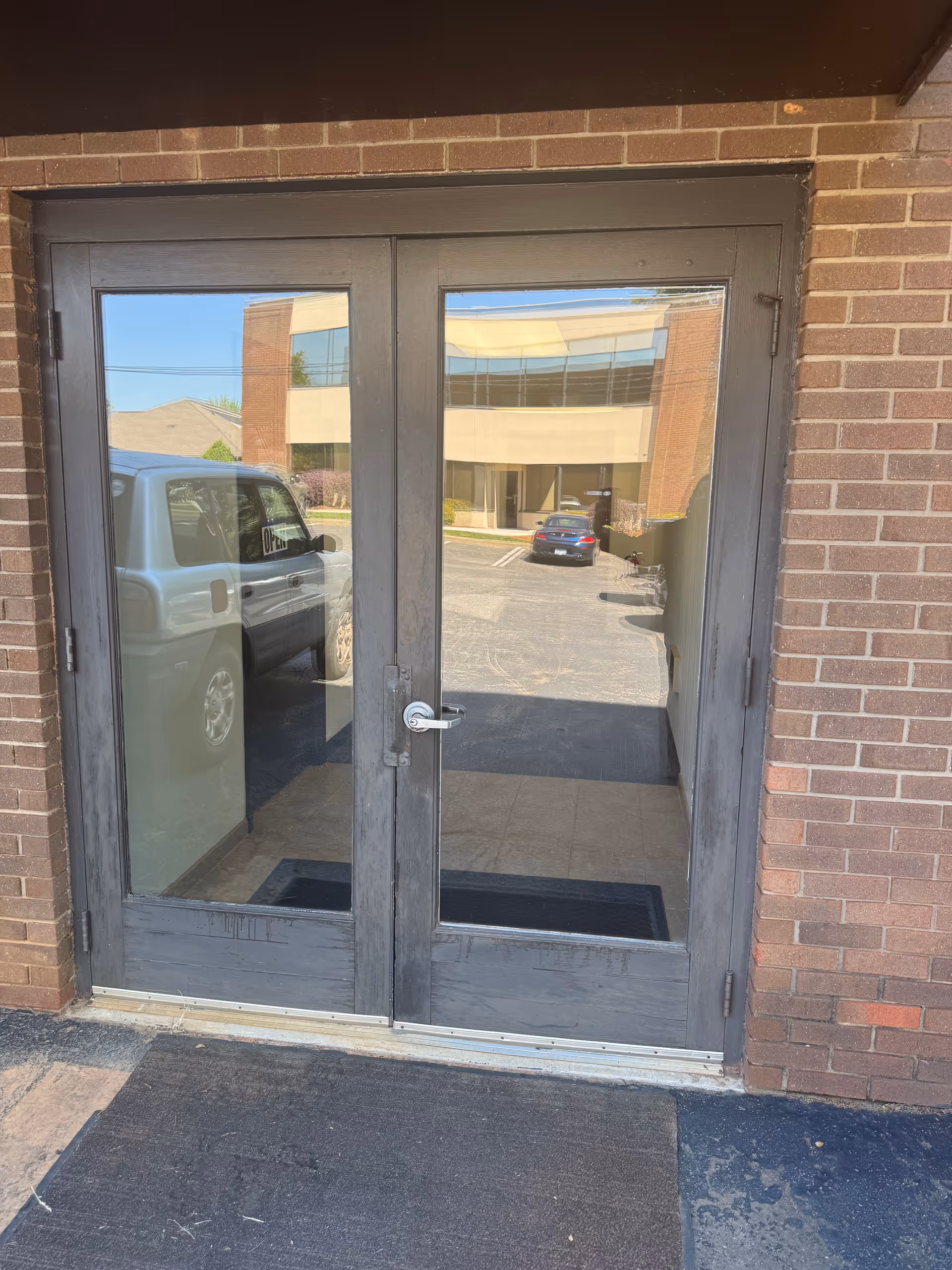 Double glass doors with dark metal frames, brick exterior, reflecting a parking lot.