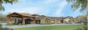 Exterior view of a single-story senior living facility building with a covered entrance and a driveway in front, surrounded by green grass and trees under a blue sky with some clouds.