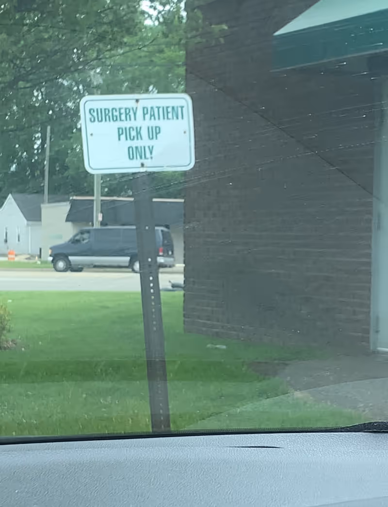Outdoor shot of a sign reading Surgery Patient Pick Up Only near a brick building.