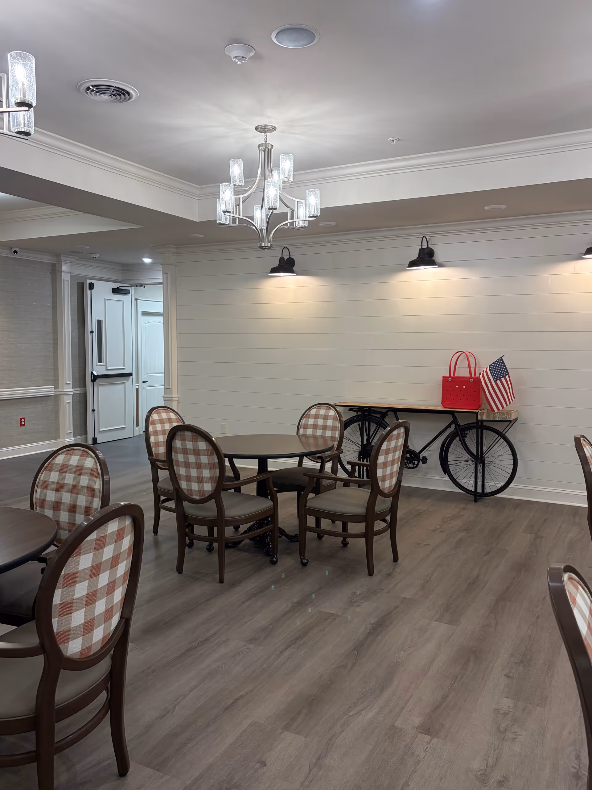 Interior dining room with round tables, checkered chairs, and chandelier lighting.