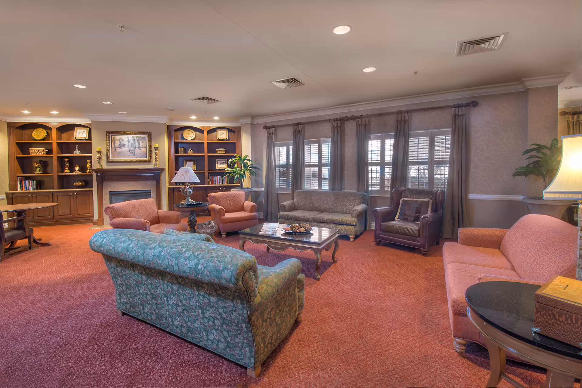 Cozy senior living lounge with sofas, a coffee table, built-in bookshelves, and a fireplace.